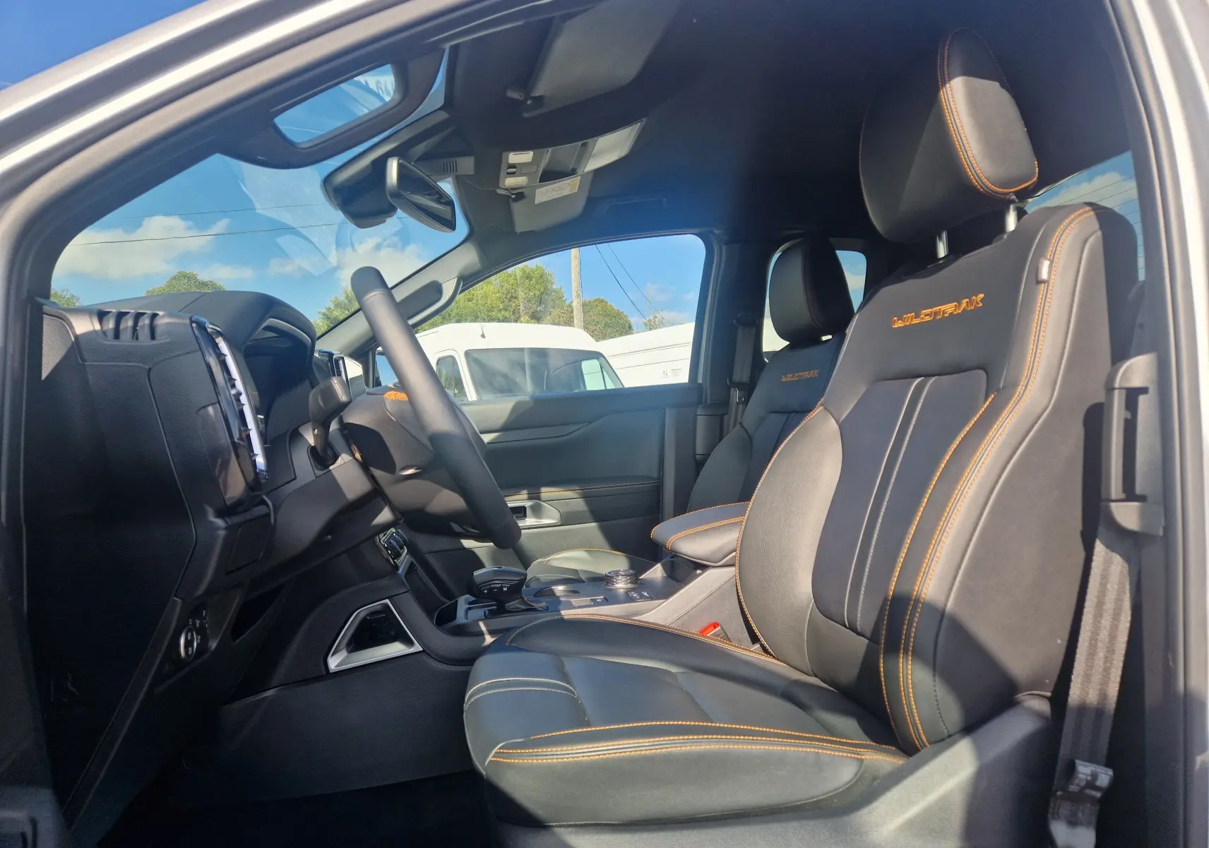 Vue intérieure arrière du Ford Ranger Super Cabine 2025, sièges noirs avec surpiqûres orange et vitre arrière donnant sur la benne.