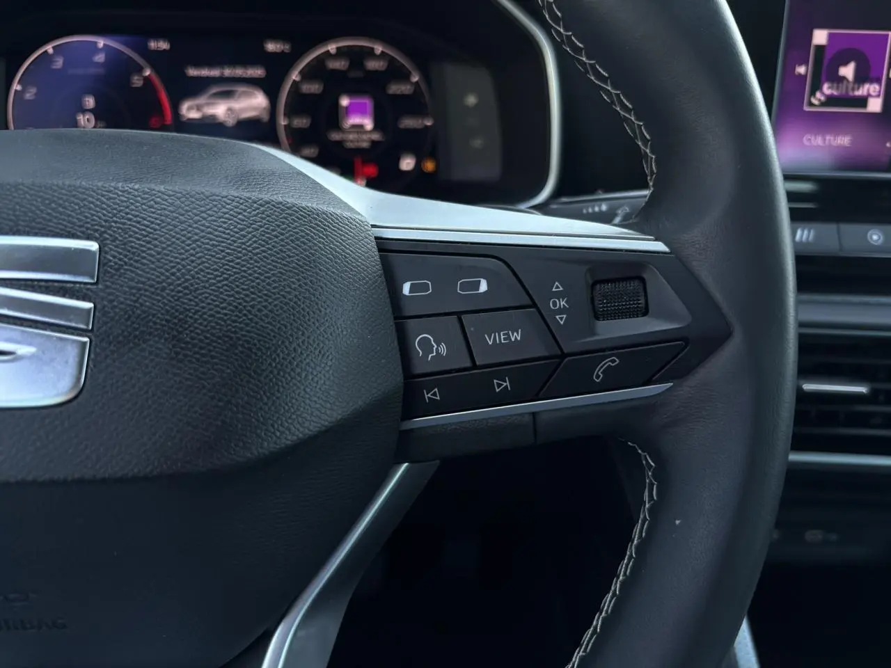 Gros plan sur le volant cuir multifonction de la SEAT LEON 2024 avec commandes intégrées et tableau de bord numérique en arrière-plan