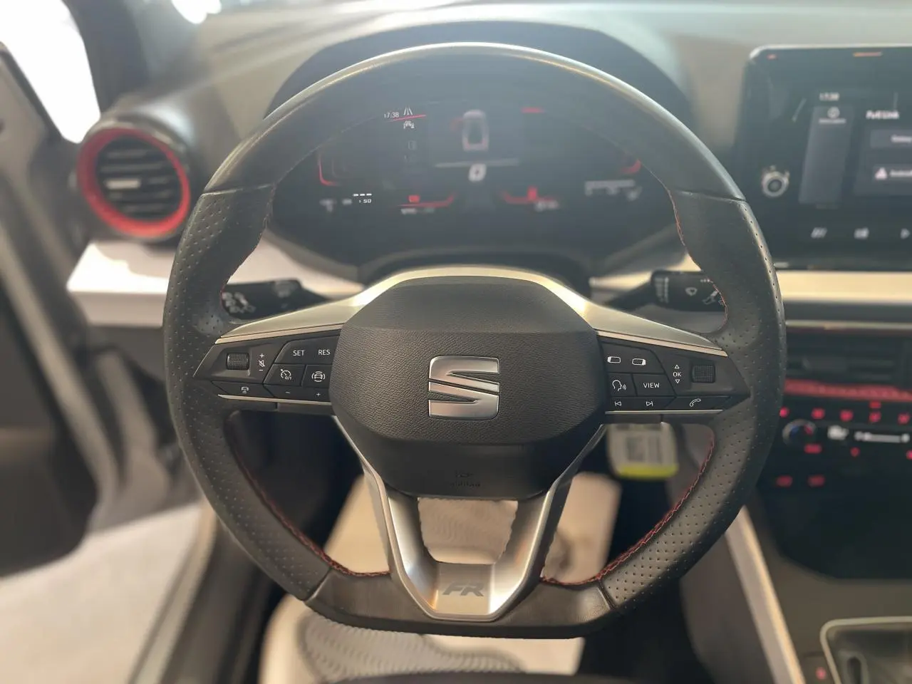 Vue rapprochée du volant sport cuir noir avec surpiqûres rouges et logo SEAT sur le tableau de bord digital.