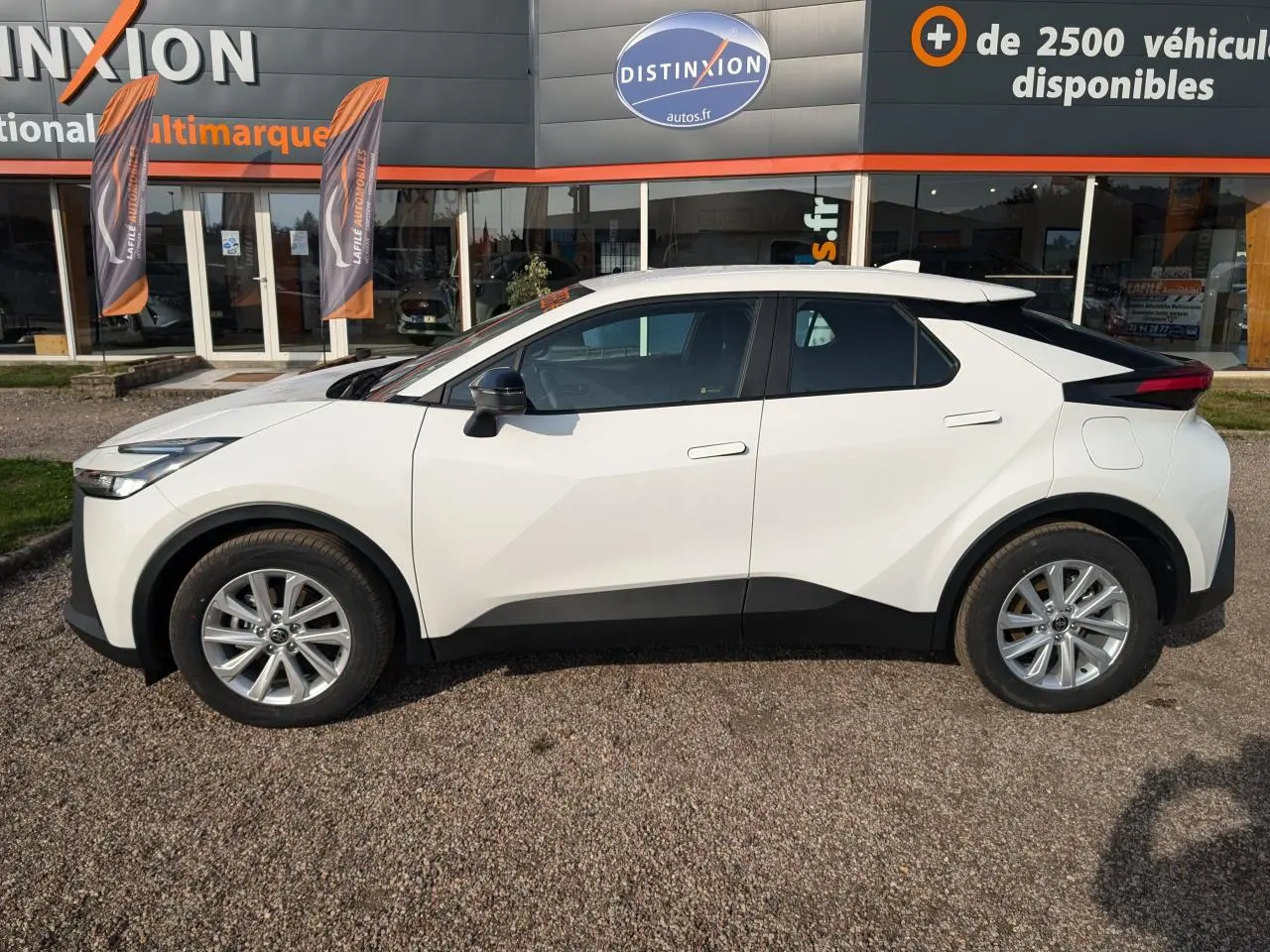 Vue de profil côté gauche du Toyota C-HR 1.8 Hybrid blanc avec jantes alliage 17 pouces sur parking extérieur.