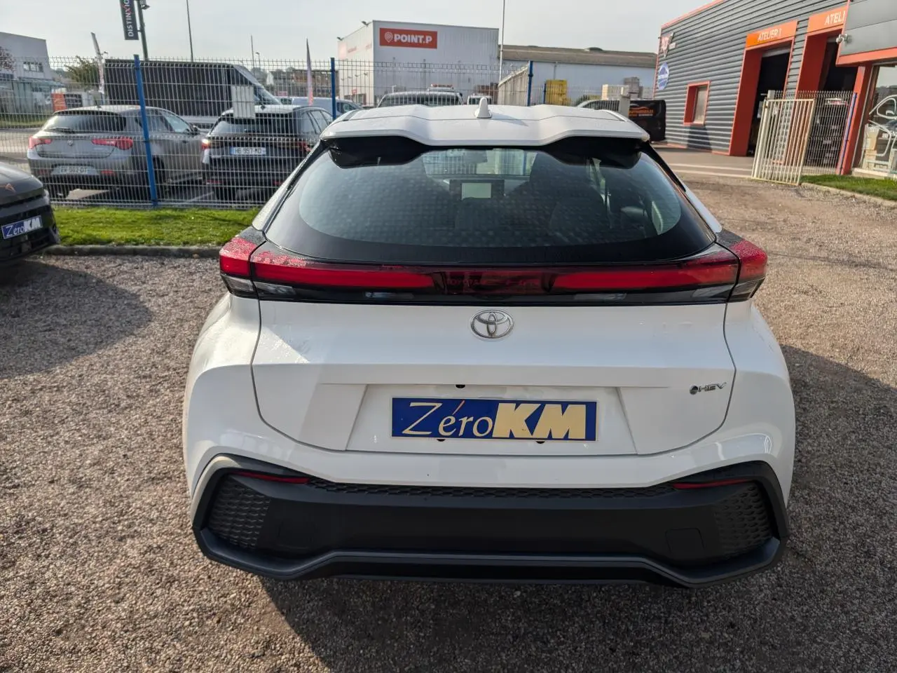 Vue arrière d'un Toyota C-HR blanc 2024 avec feux arrière full LED et logo hybride visible.
