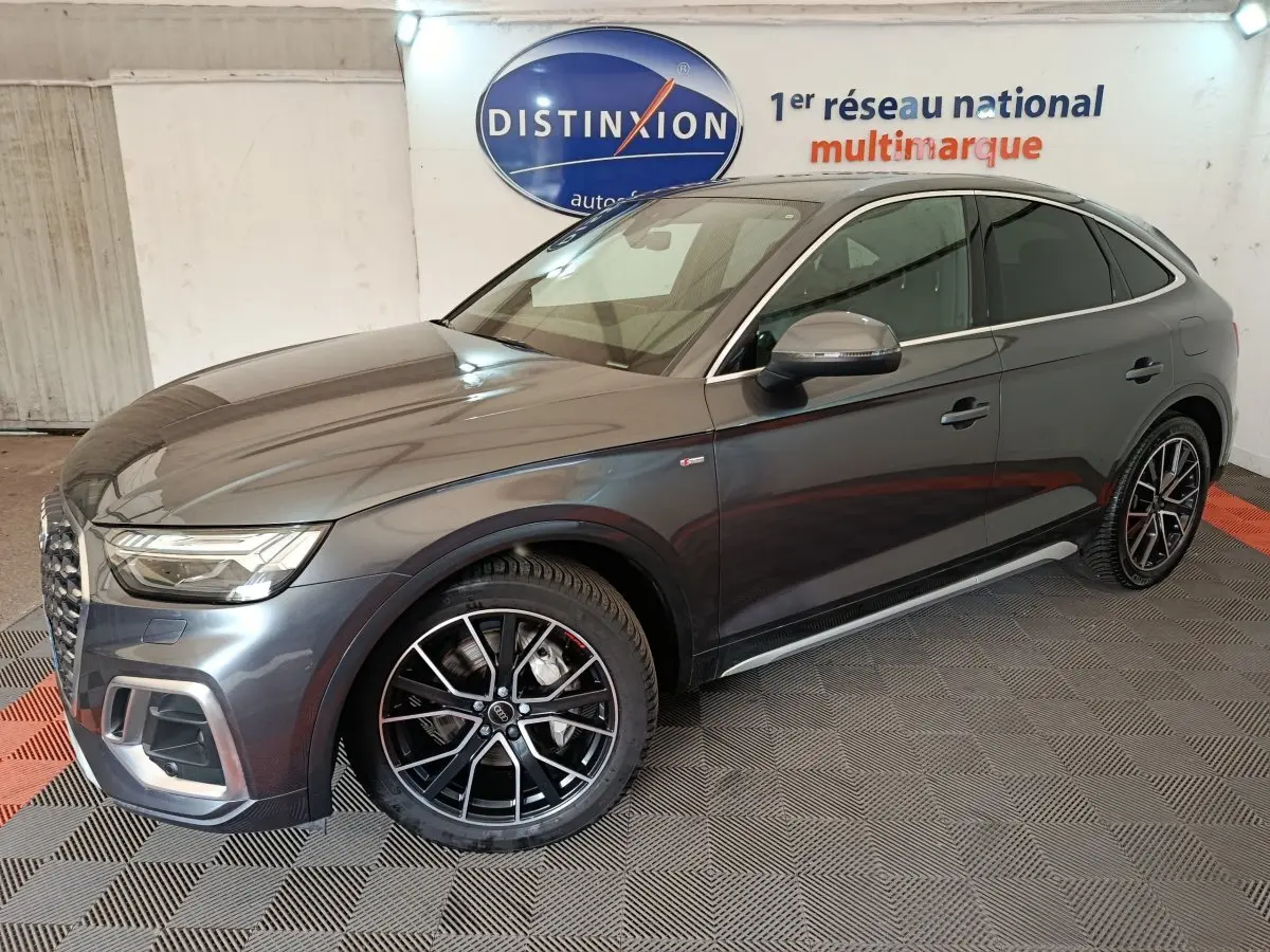 Audi Q5 gris clair 2023 en 3/4 avant droit, avec jantes noires et détails chromés, dans un showroom intérieur.