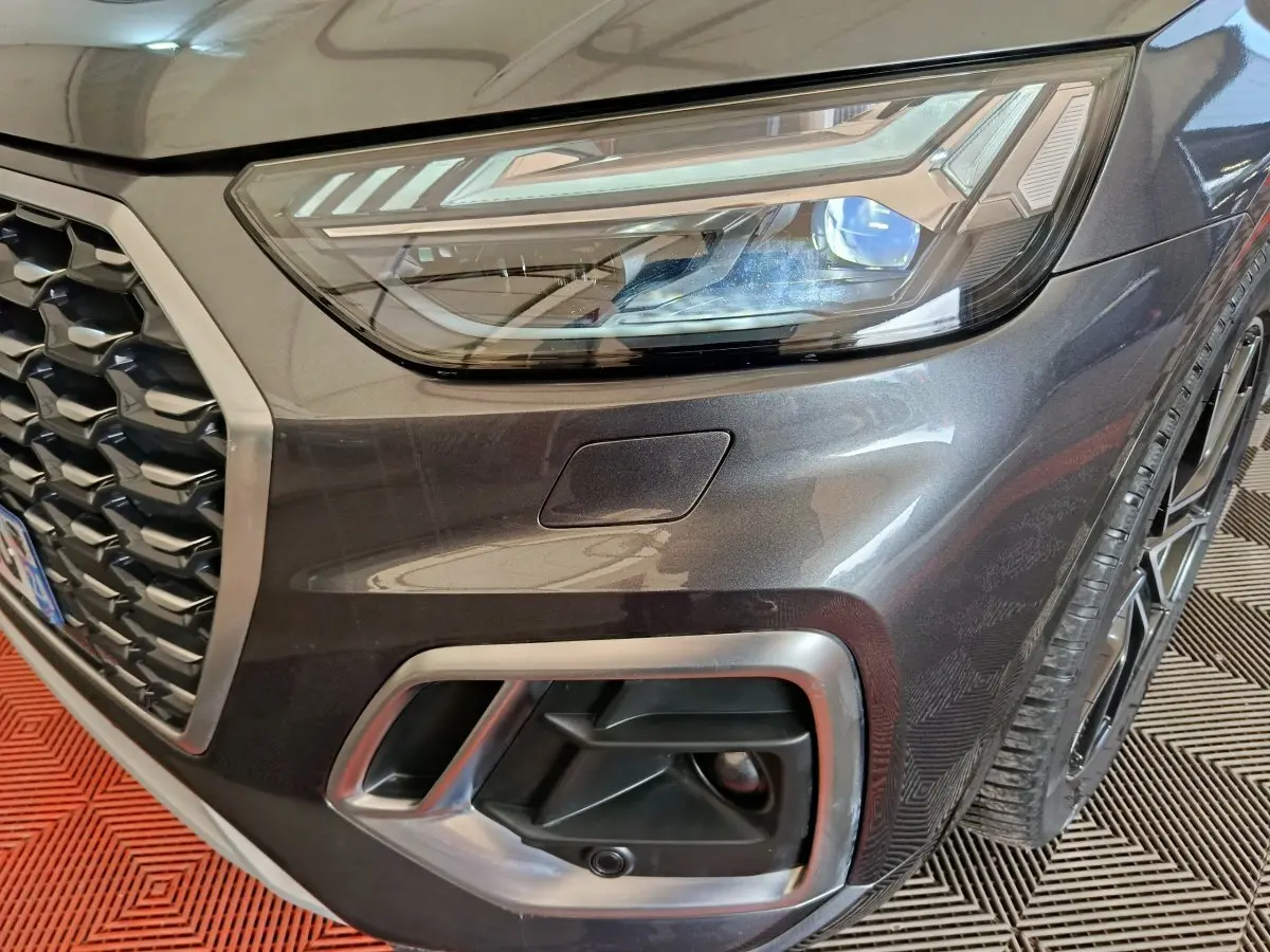 Gros plan sur l'avant droit gris clair de l'Audi Q5 2023 hybride rechargeable, mettant en valeur le phare et la calandre.