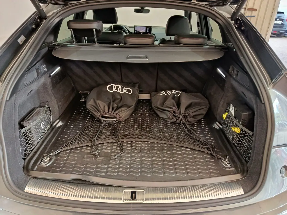Coffre ouvert d’un Audi Q5 gris clair 2023, vue arrière montrant tapis de protection et sacs noirs avec logo Audi.