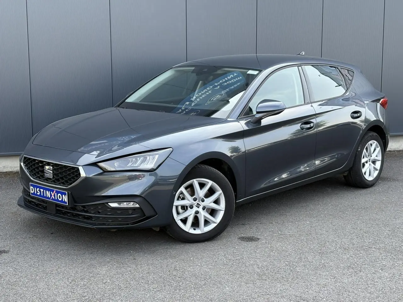 SEAT Leon 2024 gris magnétique vue 3/4 avant droit, avec jantes alliage 16 pouces et vitres arrière surteintées.