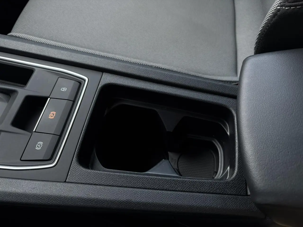 Gros plan sur la console centrale noire avec accoudoir et commandes du frein à main électrique dans SEAT Leon gris.