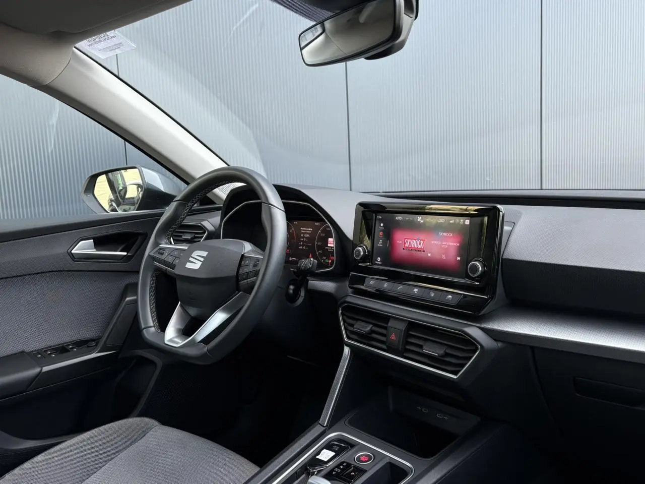 Intérieur du SEAT Leon 2024 vu côté conducteur, volant cuir multifonctions et écran tactile affichant Skyrock.