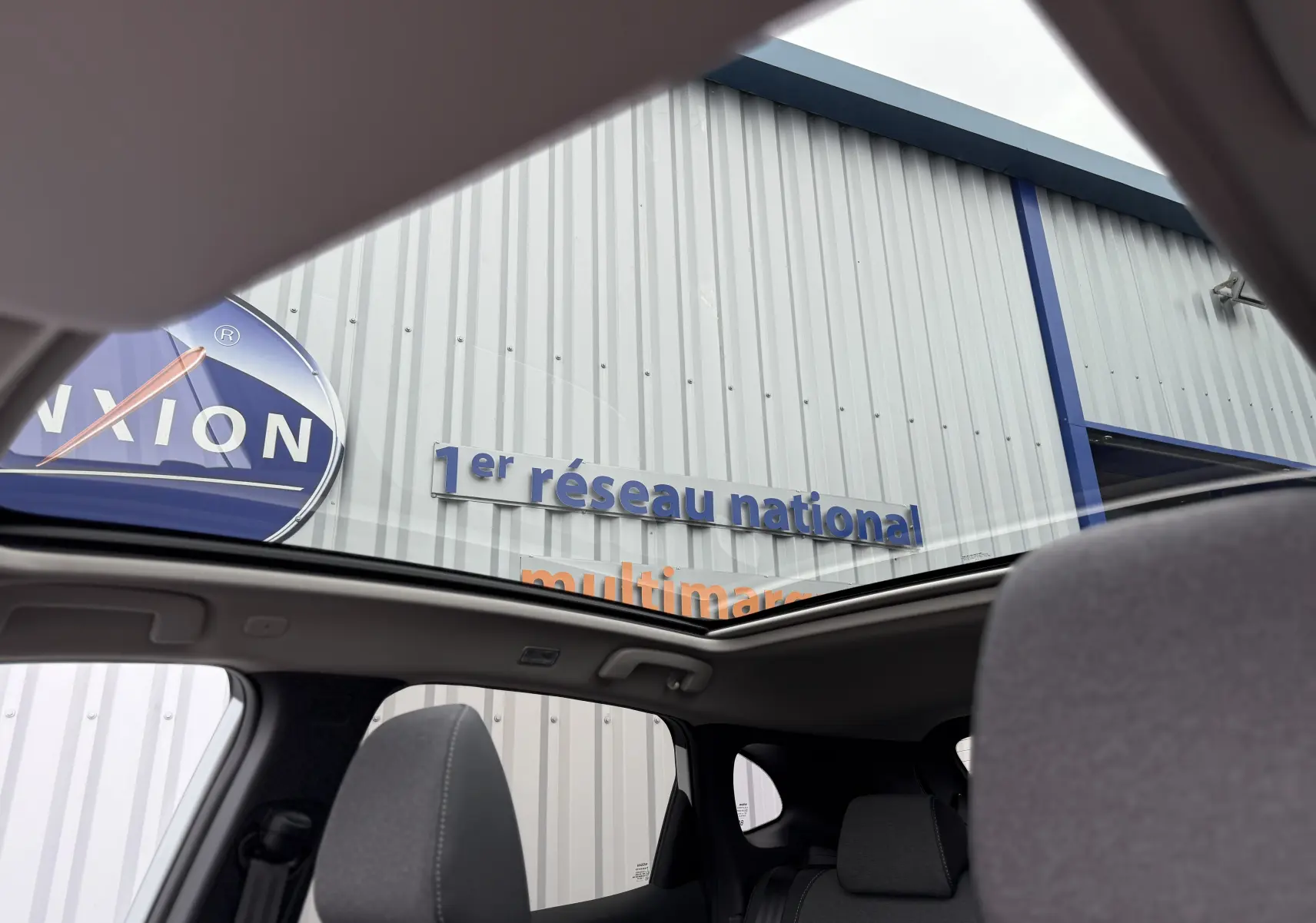 Vue intérieure du Nissan Qashqai 2025 blanc nacré, montrant le toit ouvrant panoramique et sièges gris.