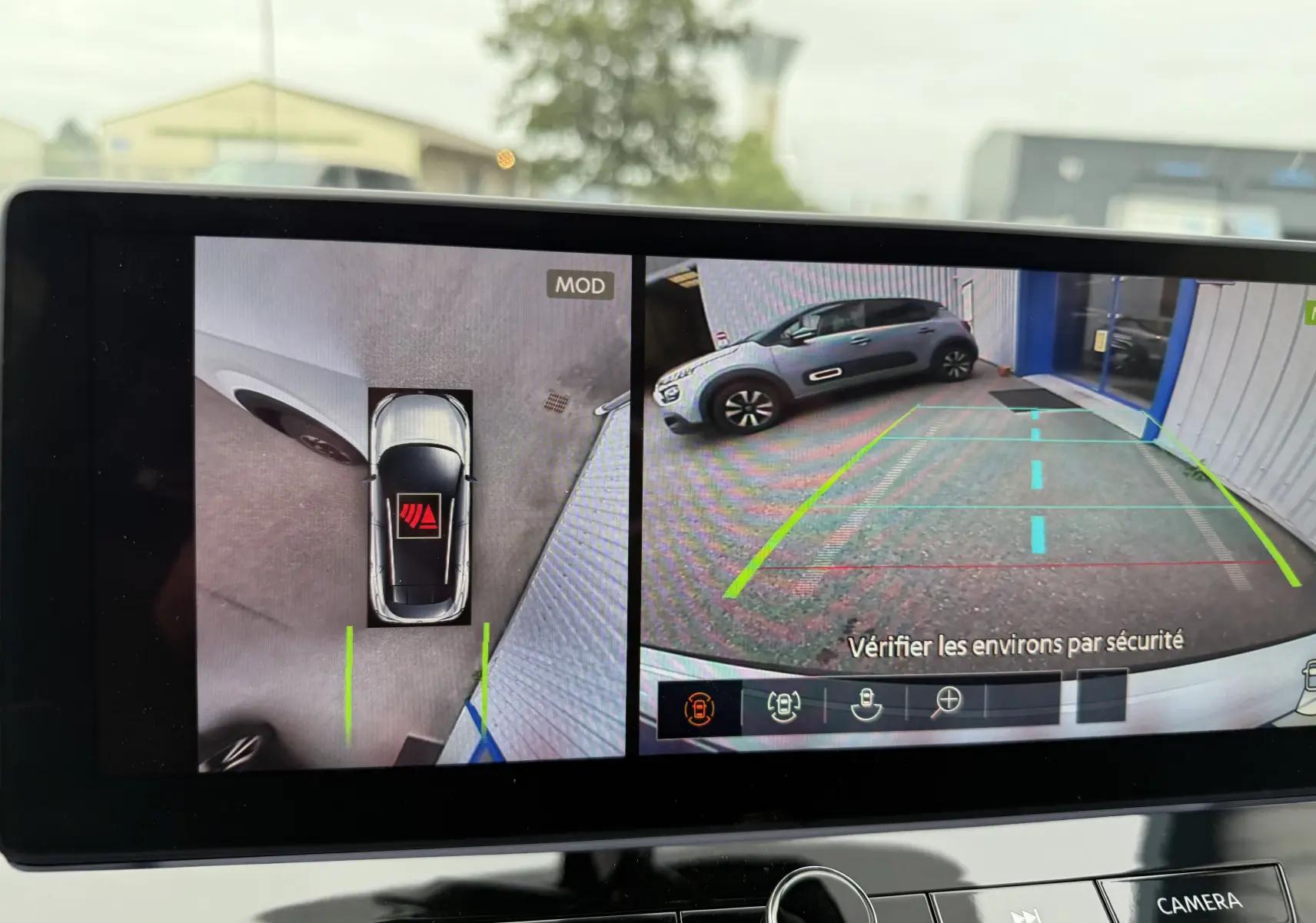 Vue écran caméra 360 du Nissan Qashqai blanc nacré, montrant l'arrière et le côté droit en stationnement.