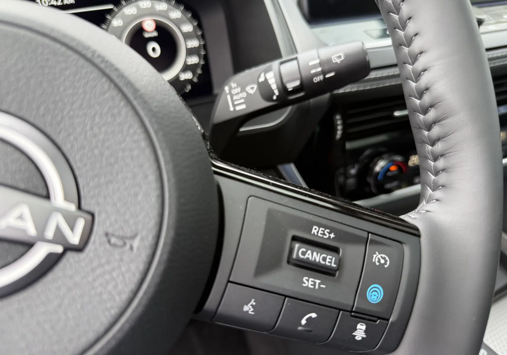 Gros plan sur le volant cuir gris du Nissan Qashqai 2025 avec commandes de régulateur de vitesse et tableau de bord numérique en arrière-plan.