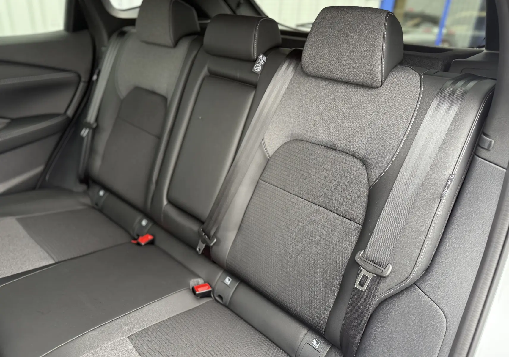 Vue rapprochée des sièges arrière gris foncé du Nissan Qashqai 2025, montrant les ceintures de sécurité et appuie-têtes.