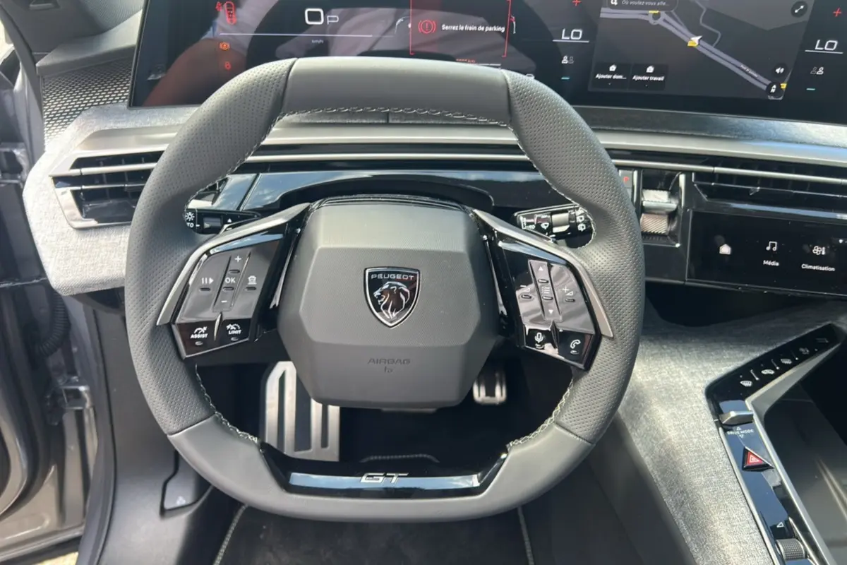 Vue rapprochée du volant GT du Peugeot 5008 Hybrid 145 gris artense, avec tableau de bord numérique et commandes intégrées.