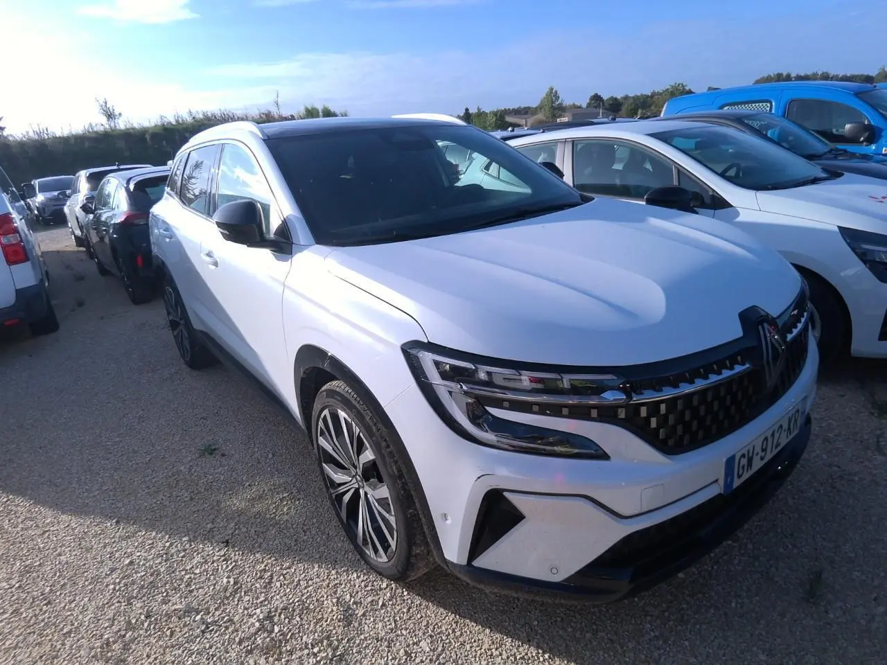Renault Austral blanc nacré vu en 3/4 avant droit, avec calandre à damier noire et jantes alliage 20 pouces.
