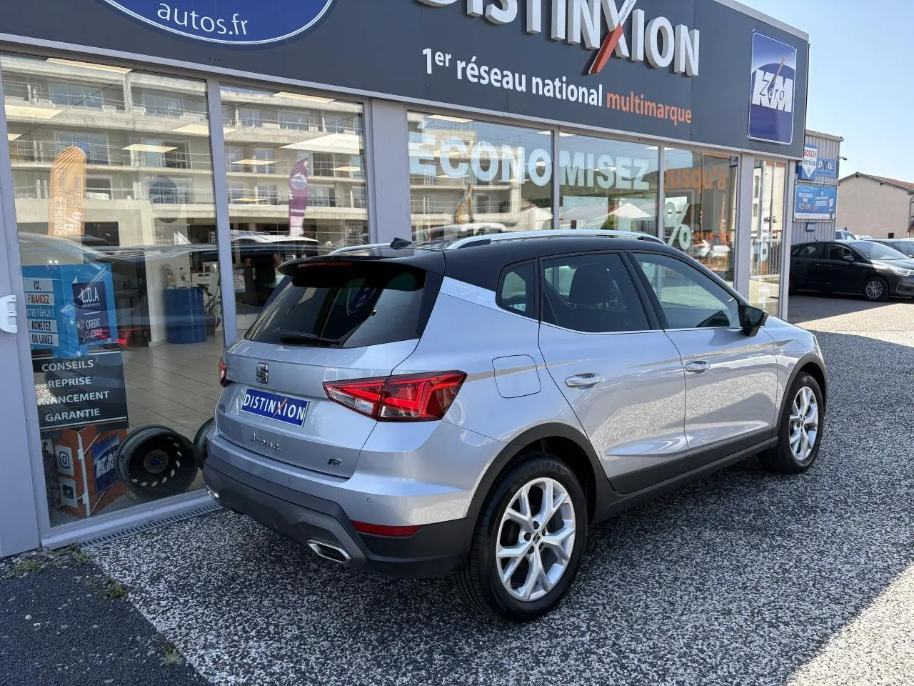 SEAT Arona 2024 gris GRS en 3/4 arrière droit, avec jantes alliage et feux arrière LED visibles devant un showroom.