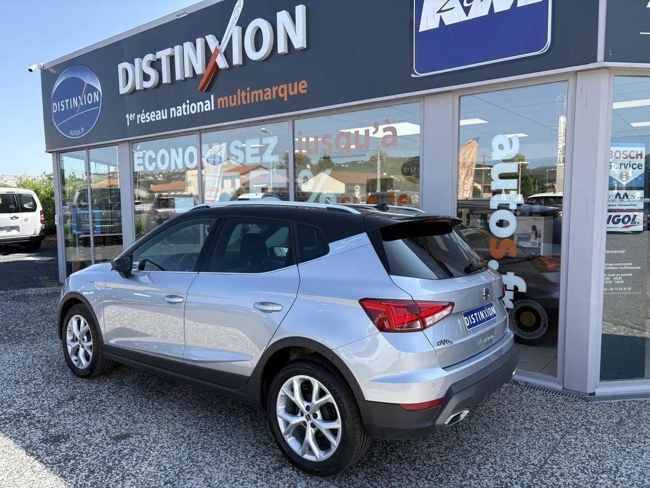 Vue 3/4 arrière droite d’un SEAT Arona 2024 gris clair avec jantes alliage et vitres teintées, devant un showroom.