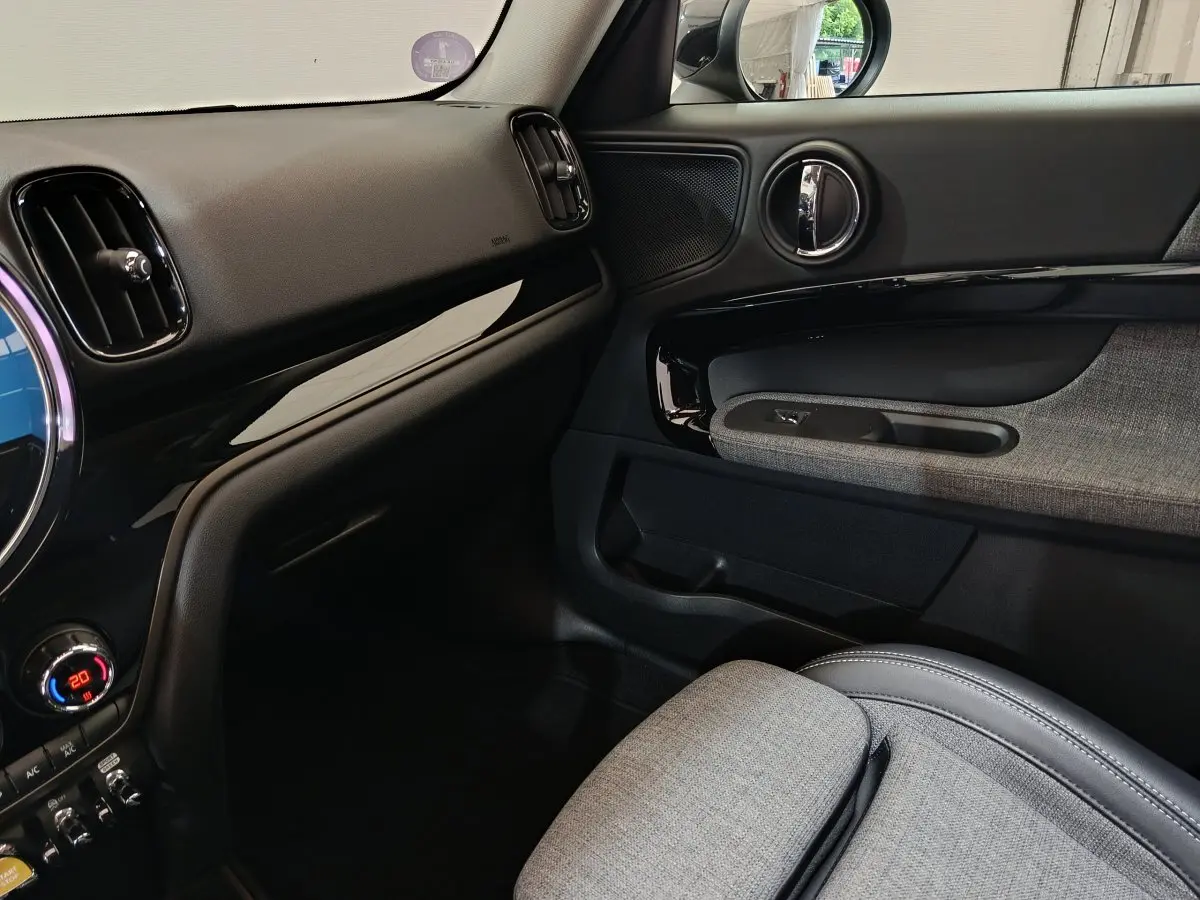 Intérieur côté passager du MINI Countryman blanc, montrant la porte avec garniture grise et tableau de bord noir brillant.
