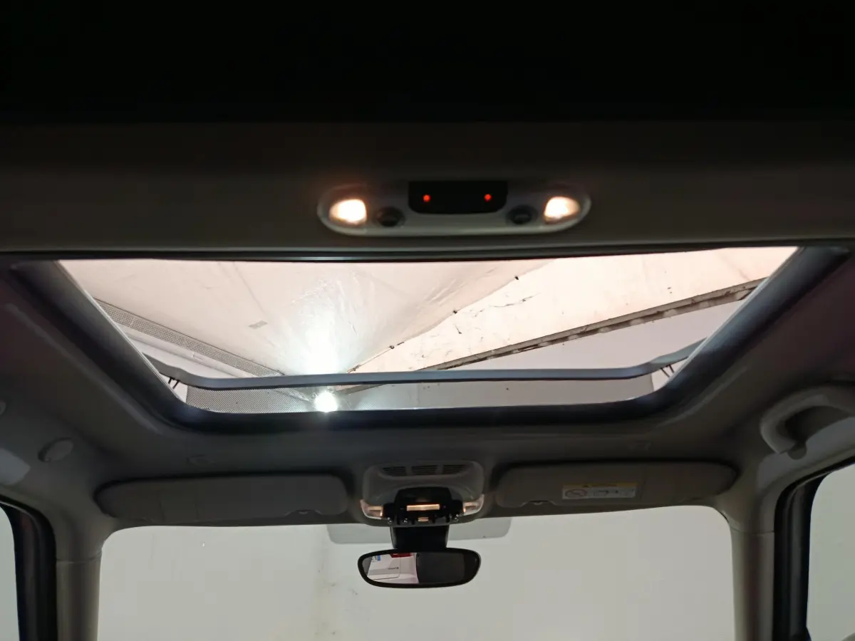 Toit ouvrant panoramique ouvert vu de l'intérieur avant du MINI Countryman blanc, éclairage intérieur allumé.