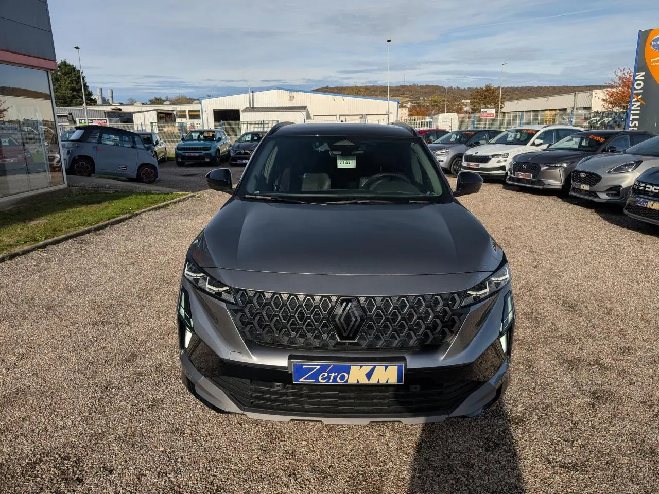 Vue avant d'un Renault Austral gris métallisé avec calandre noire et plaque Zéro KM visible en concession.