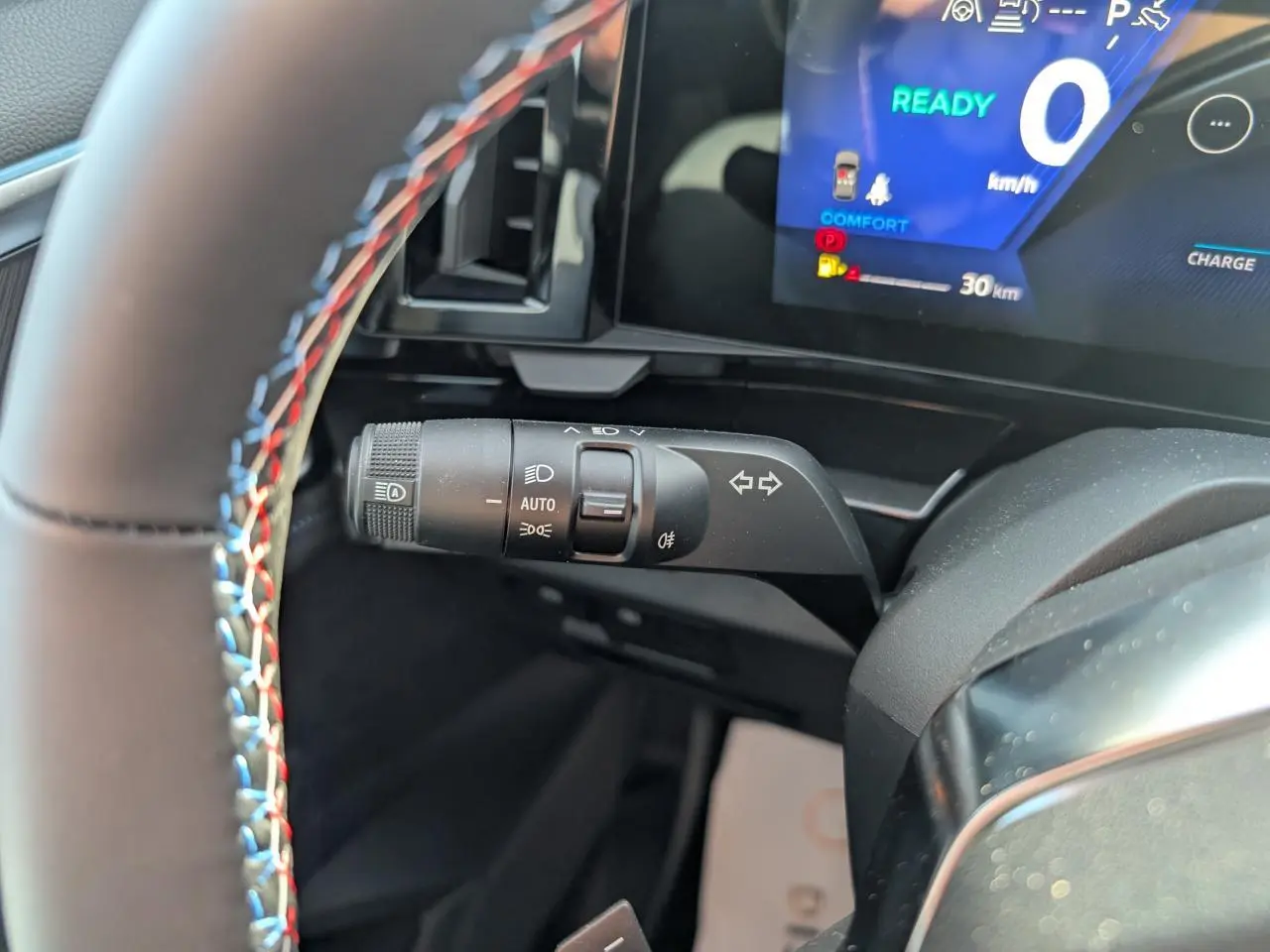 Gros plan sur la commande de clignotants du Renault Austral gris, volant avec surpiqûres tricolores et tableau de bord numérique.