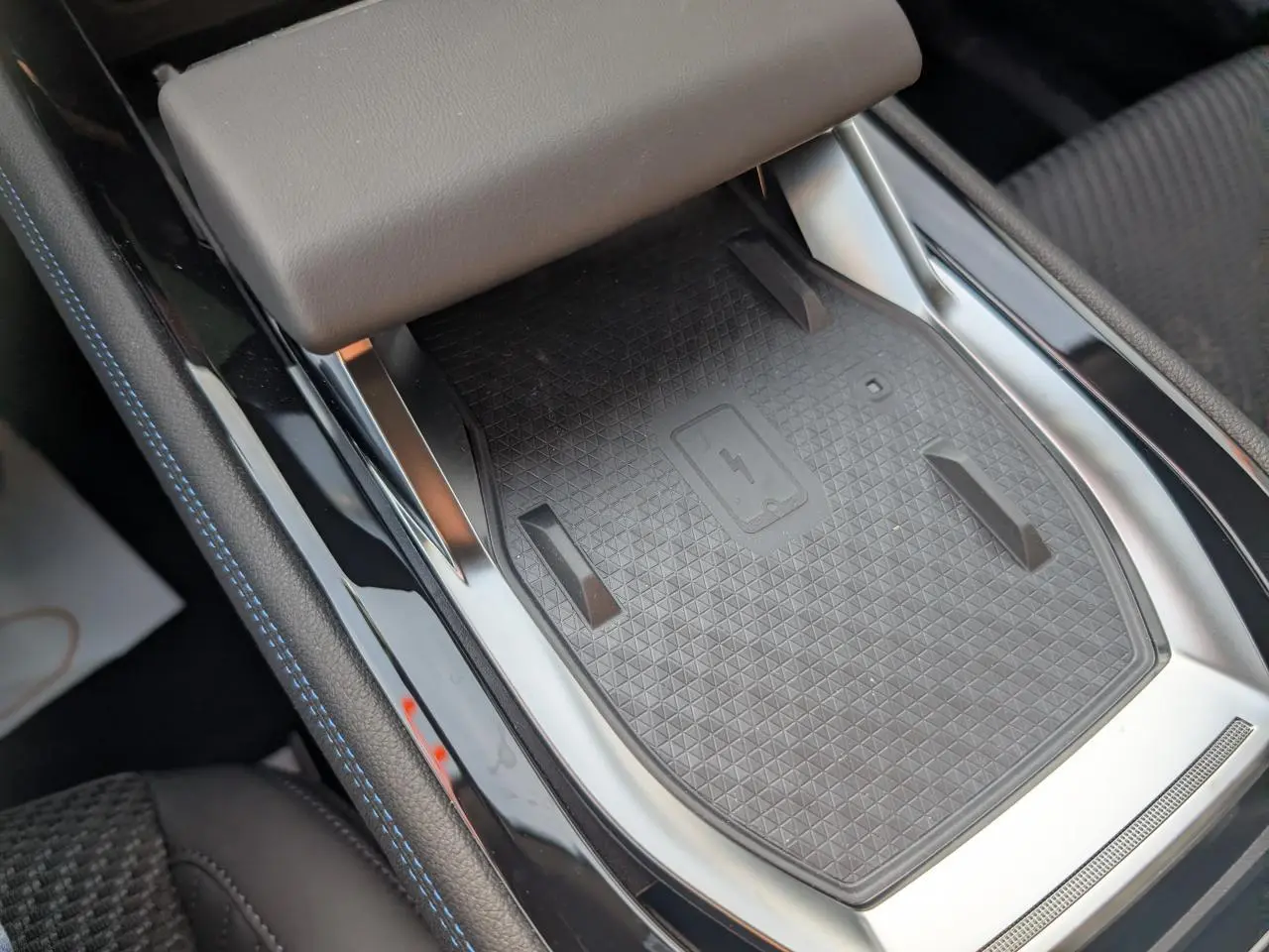 Vue rapprochée du chargeur smartphone à induction noir avec surpiqûres bleues sur la console centrale du Renault Austral gris métallisé.
