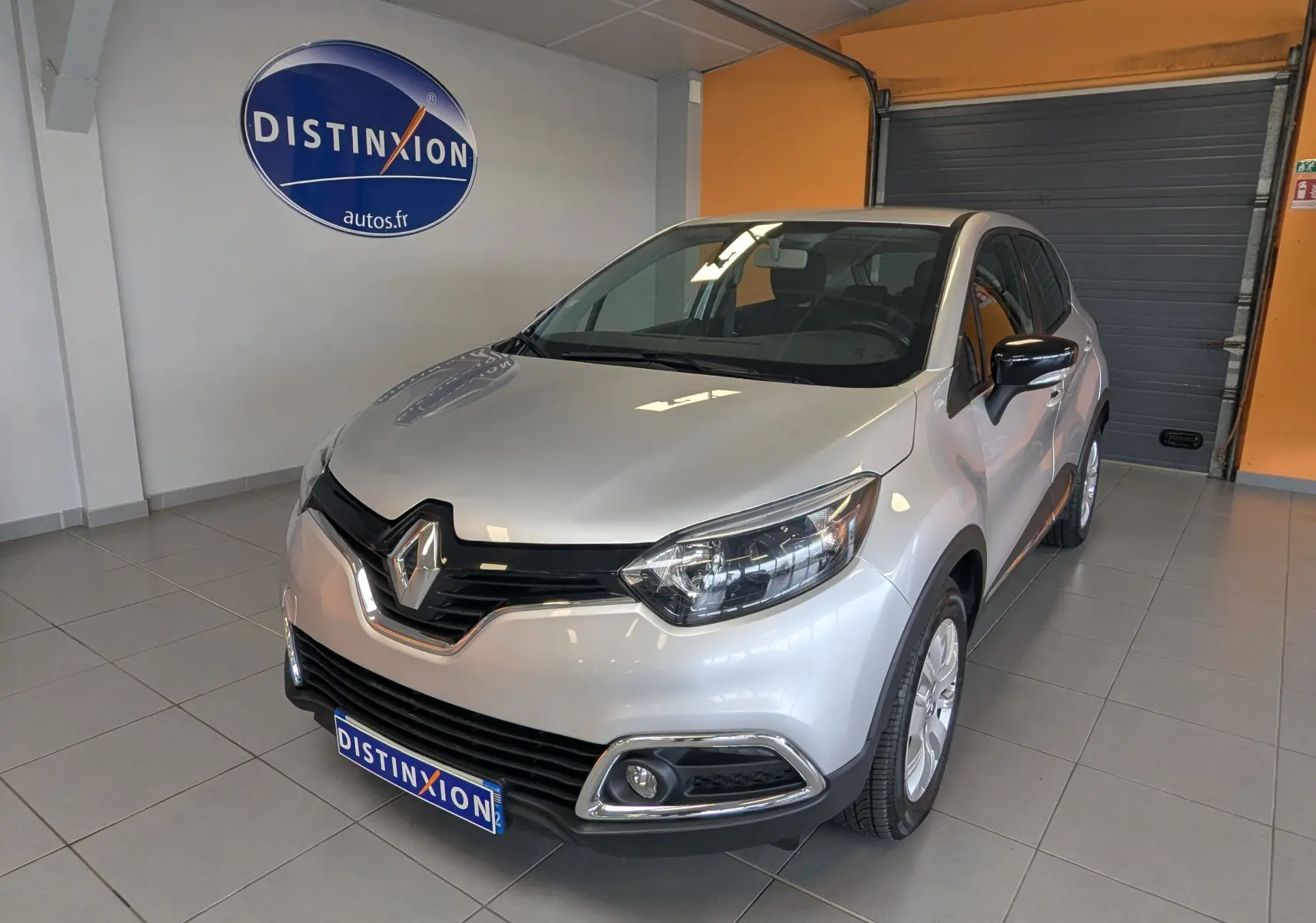 Renault Captur gris clair vue 3/4 avant droit en intérieur avec logo Distinxion en arrière-plan.