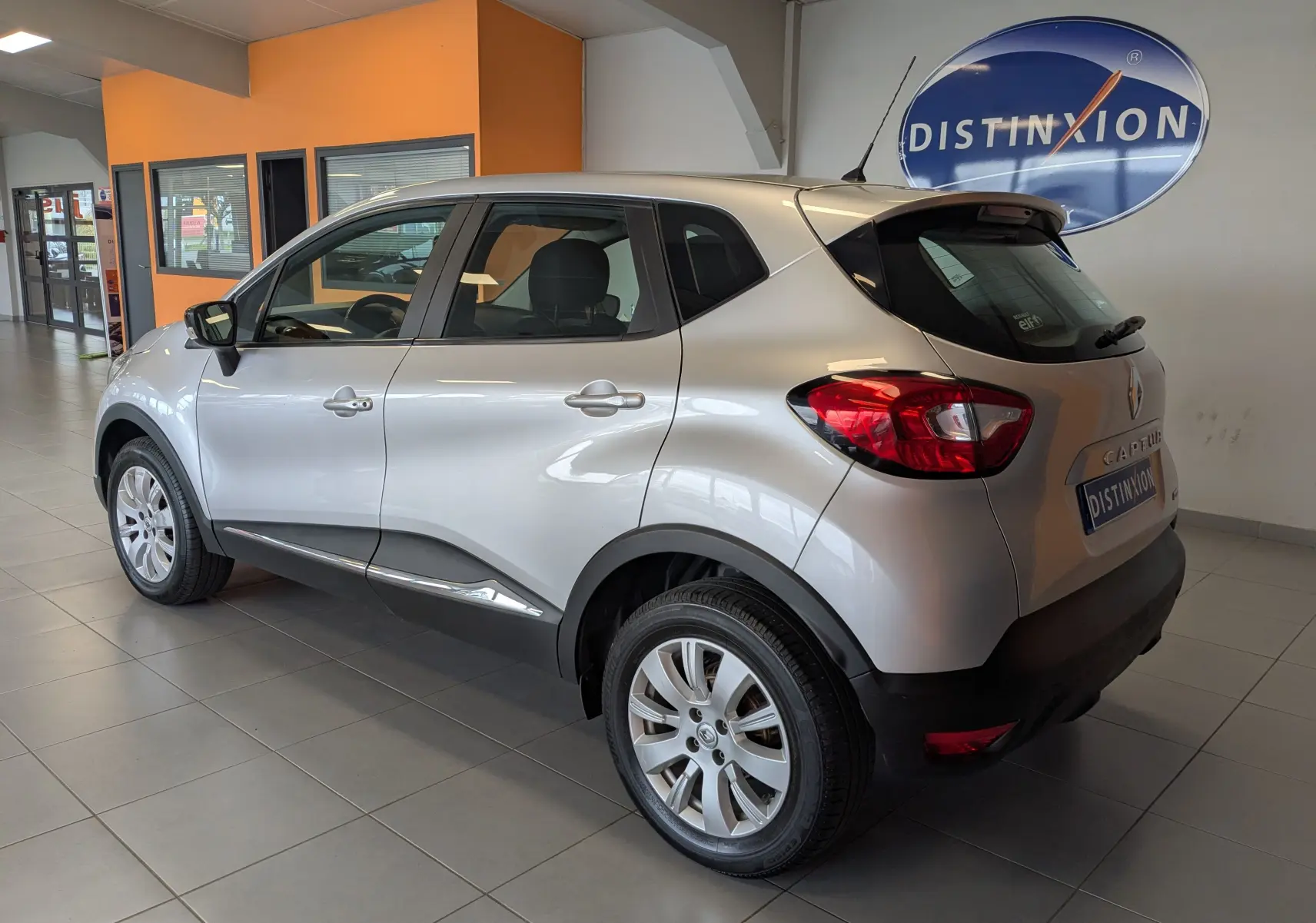 Vue 3/4 arrière droite d'un Renault Captur gris clair 2017 en intérieur, avec jantes alliage et détails noirs contrastants.
