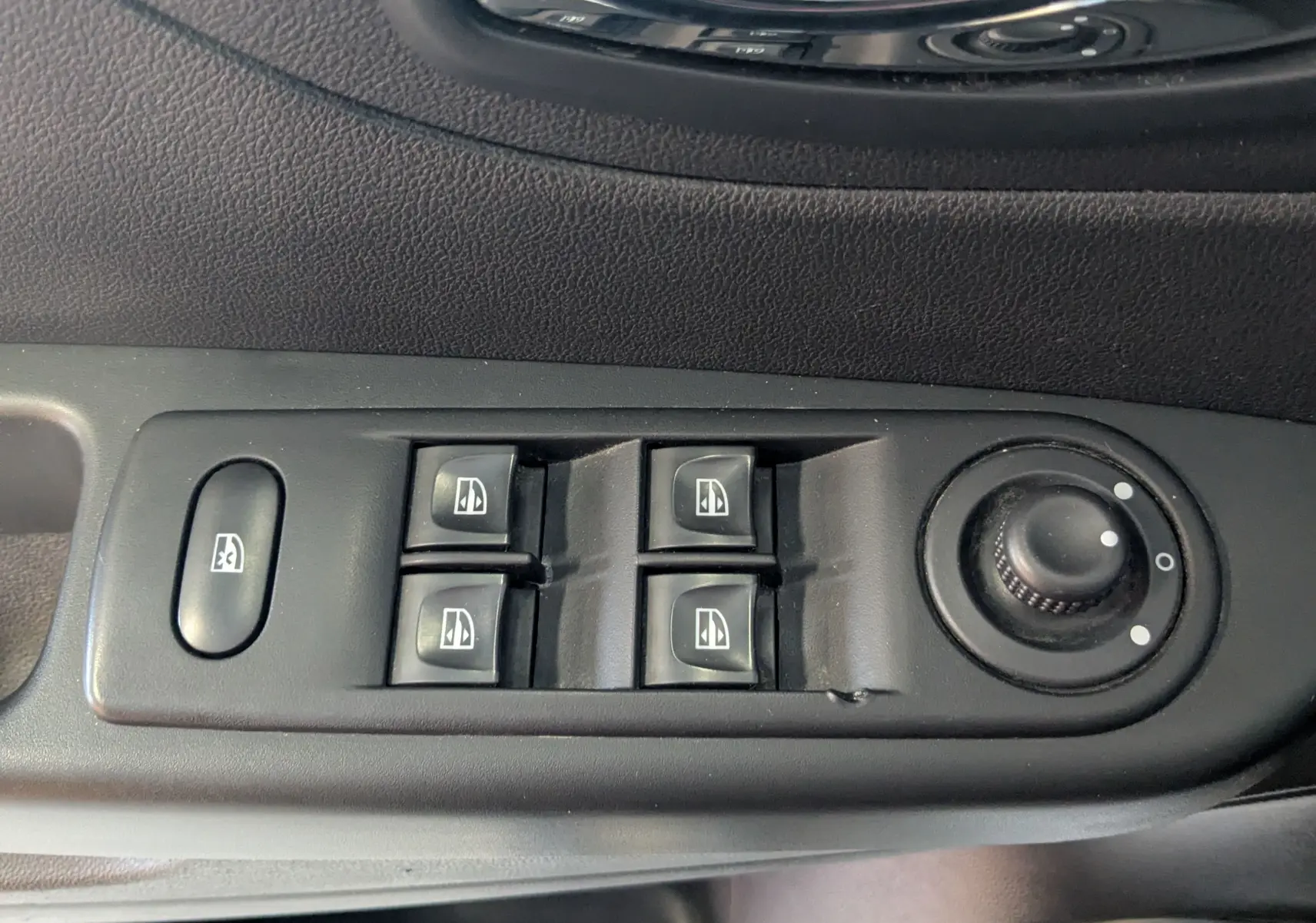 Gros plan sur les commandes de lève-vitres et réglage des rétroviseurs côté conducteur d’un Renault Captur gris clair.