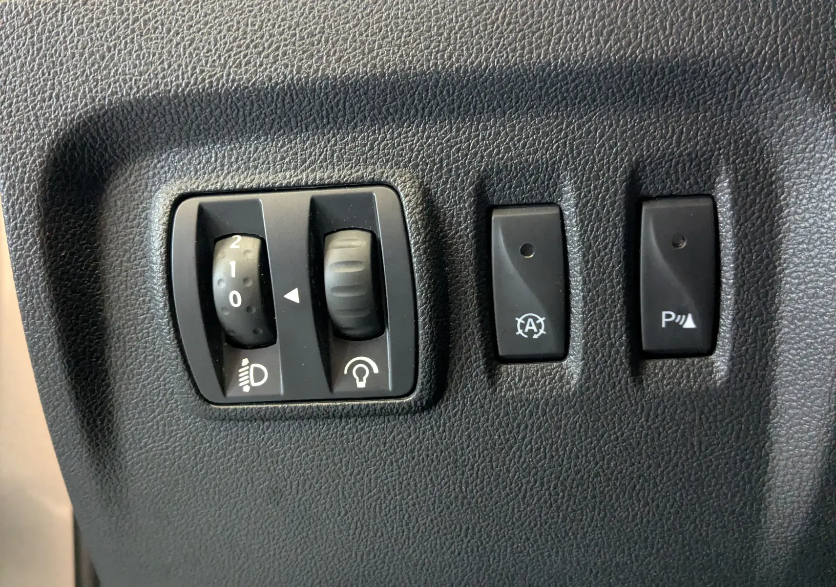 Gros plan sur les commandes intérieures noires du Renault Captur 1.5 dCi 90 Business, réglage phares et boutons de fonction.