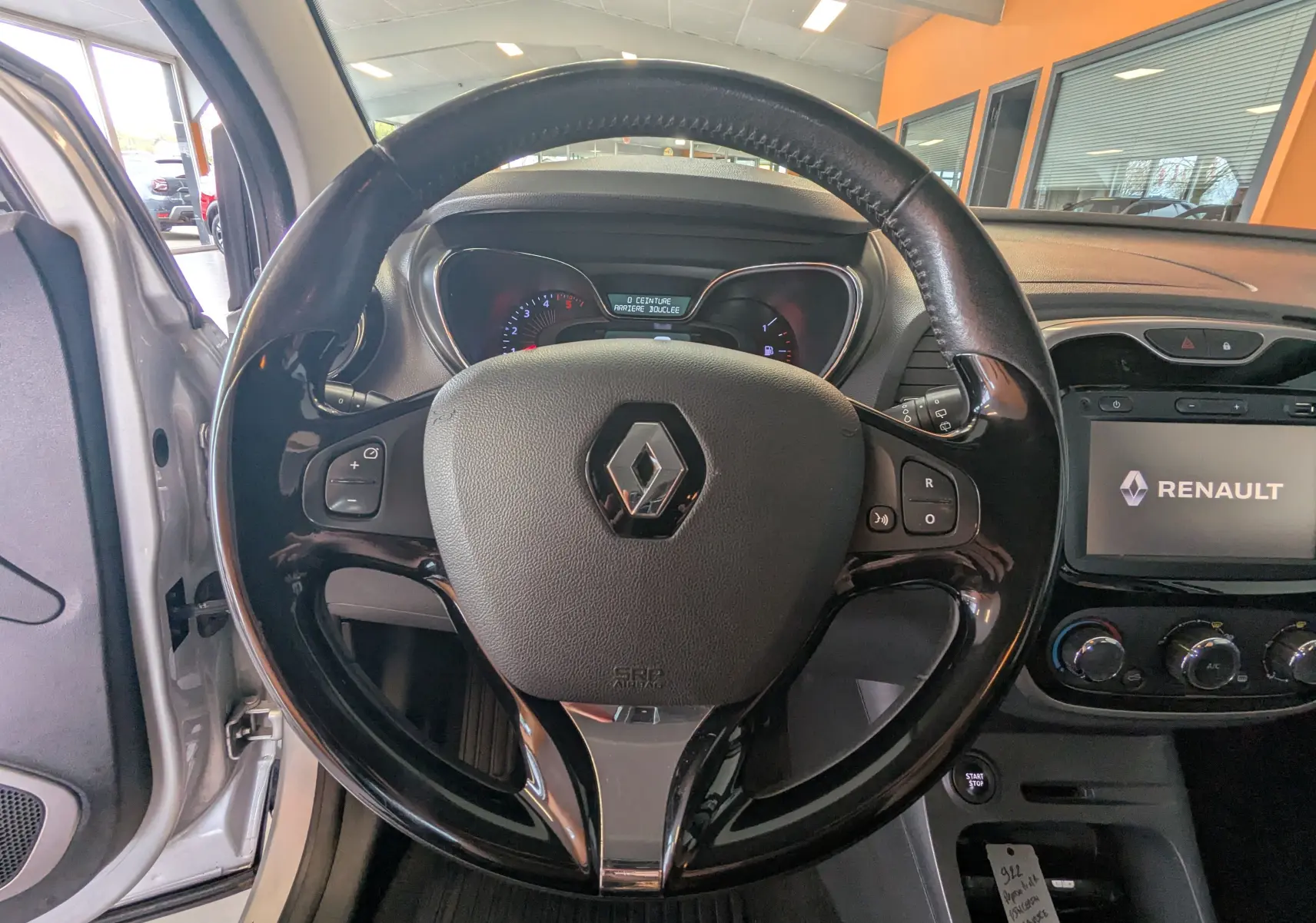 Vue intérieure centrée sur le volant noir brillant du Renault Captur gris clair, avec tableau de bord et écran multimédia visibles.