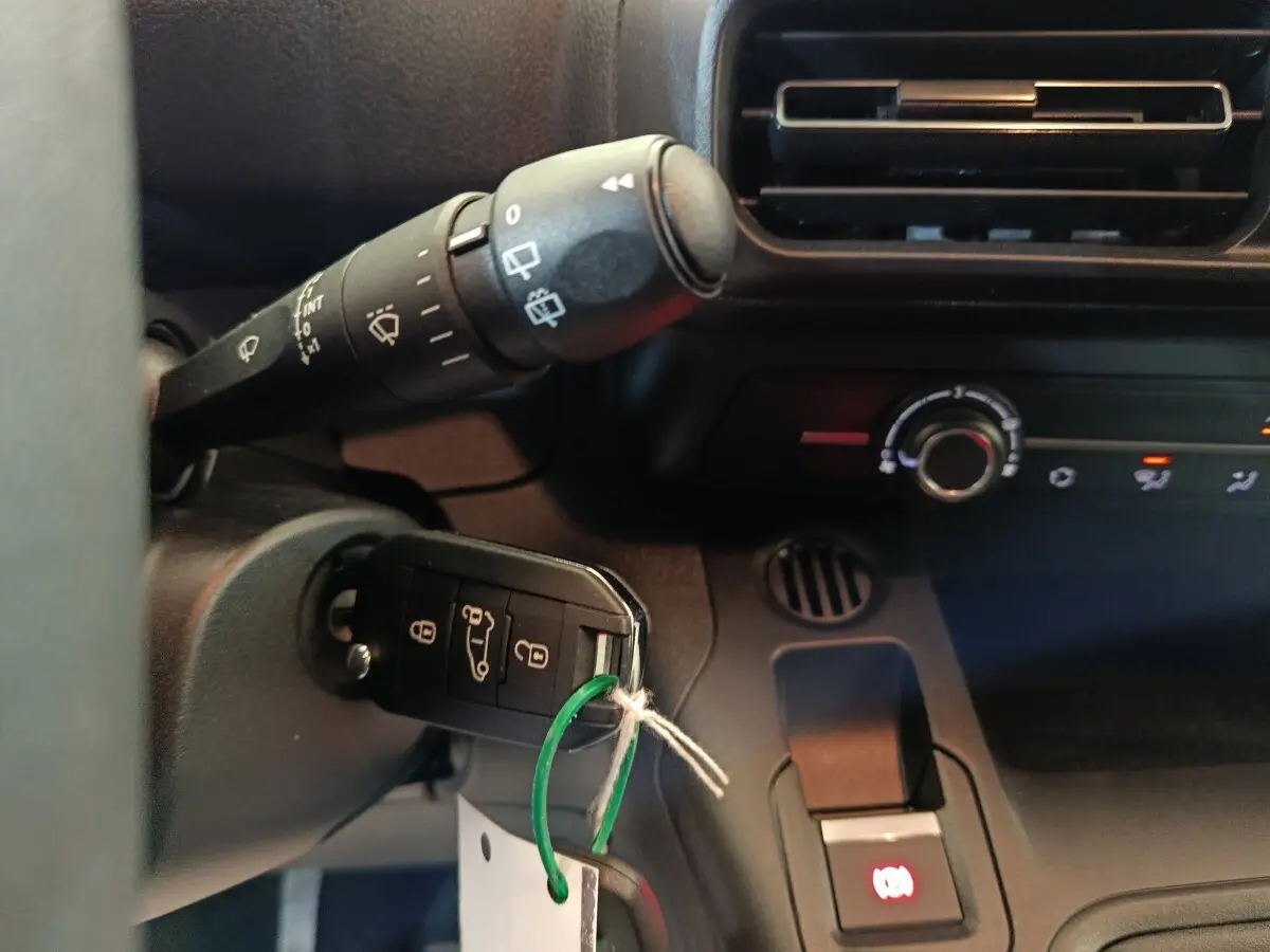 Gros plan intérieur sur la clé de contact insérée dans un Peugeot Partner blanc, avec commandes de climatisation et essuie-glace visibles.