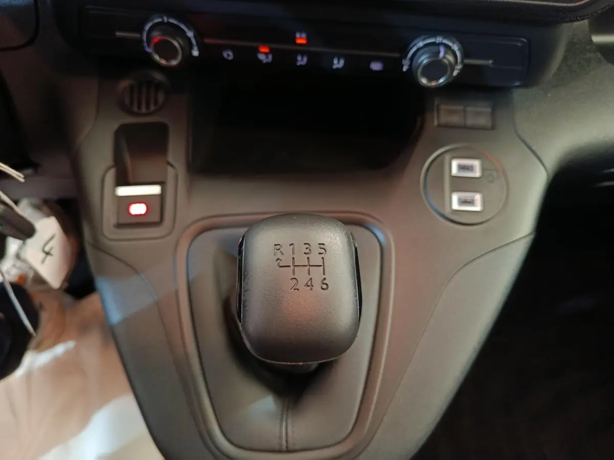 Gros plan sur le levier de vitesses manuel noir du Peugeot Partner blanc, avec commandes et ports USB visibles en arrière-plan.