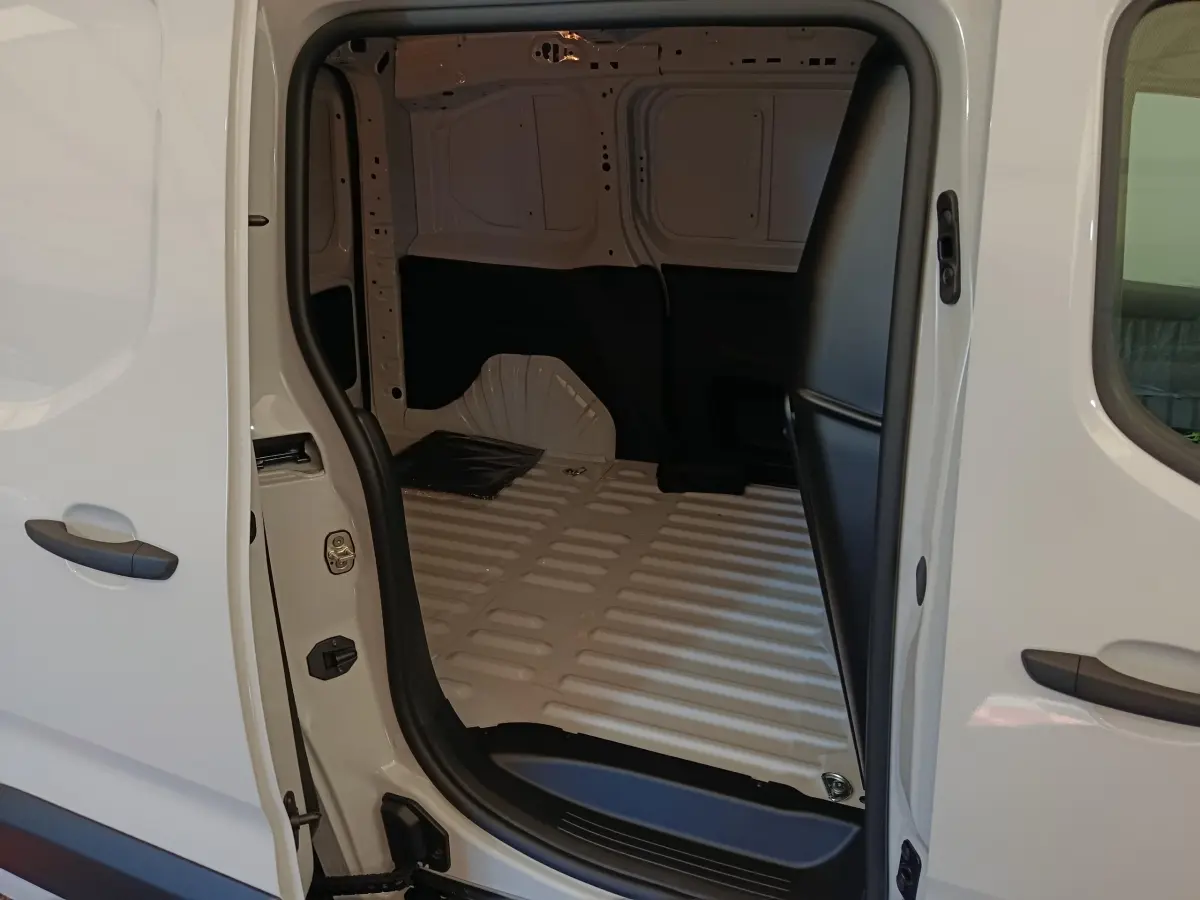 Vue intérieure côté gauche du coffre ouvert d’un Peugeot Partner blanc 2025, montrant l’espace de chargement vide.