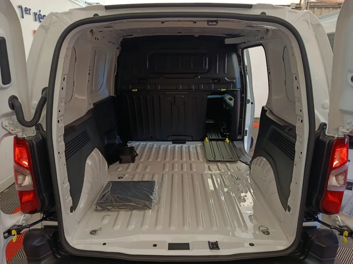 Vue arrière ouverte du Peugeot Partner blanc 2025, montrant l'espace de chargement vide avec cloison pleine noire.