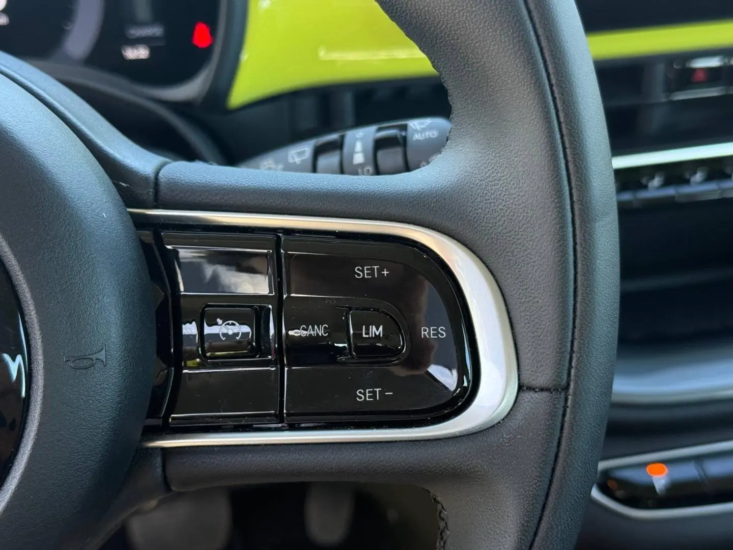 Gros plan sur les commandes de régulateur de vitesse au volant noir du Fiat 500 e jaune, intérieur moderne et épuré.
