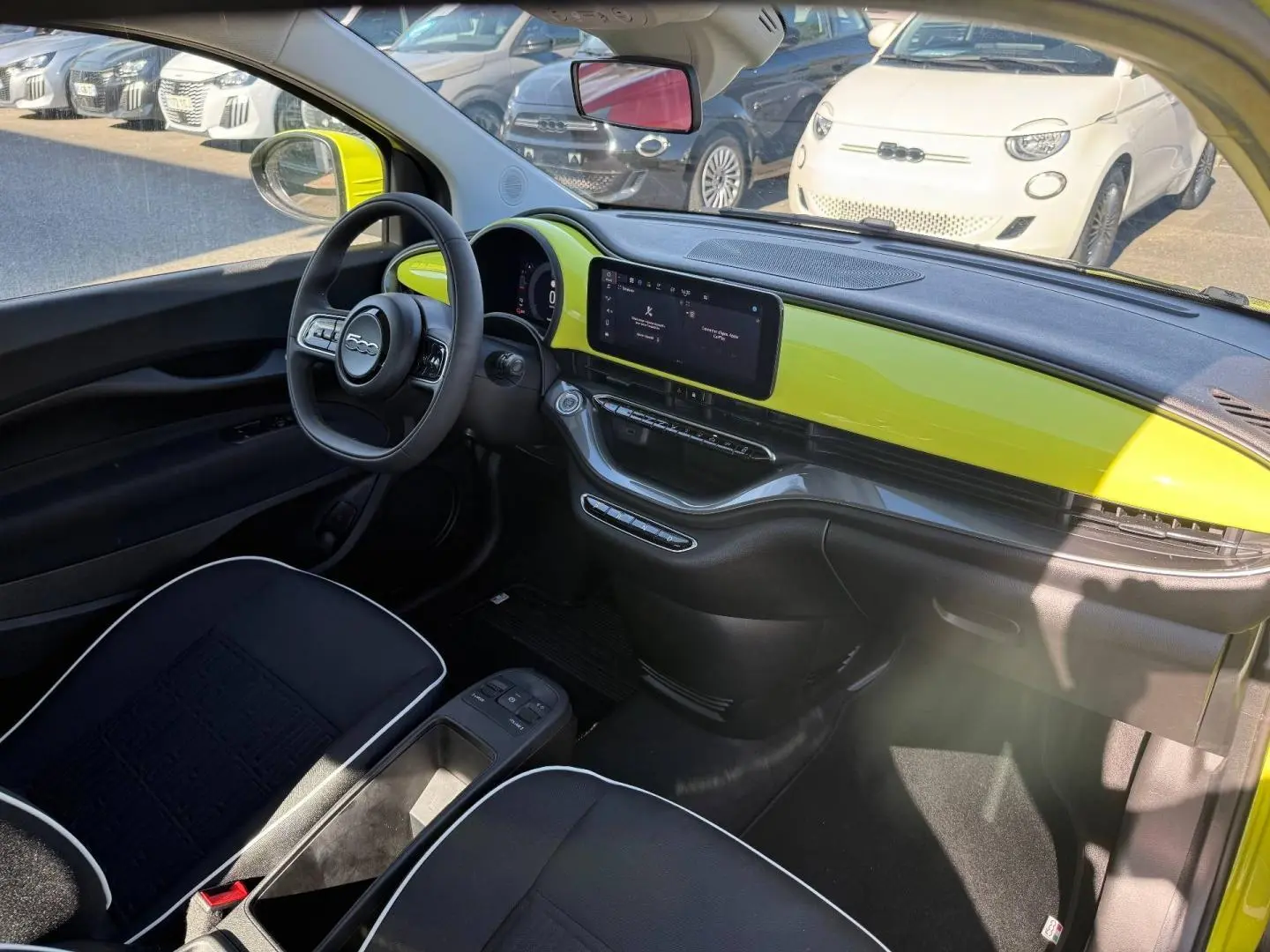 Vue intérieure côté conducteur de la Fiat 500 électrique jaune, tableau de bord avec écran tactile et volant multifonction.