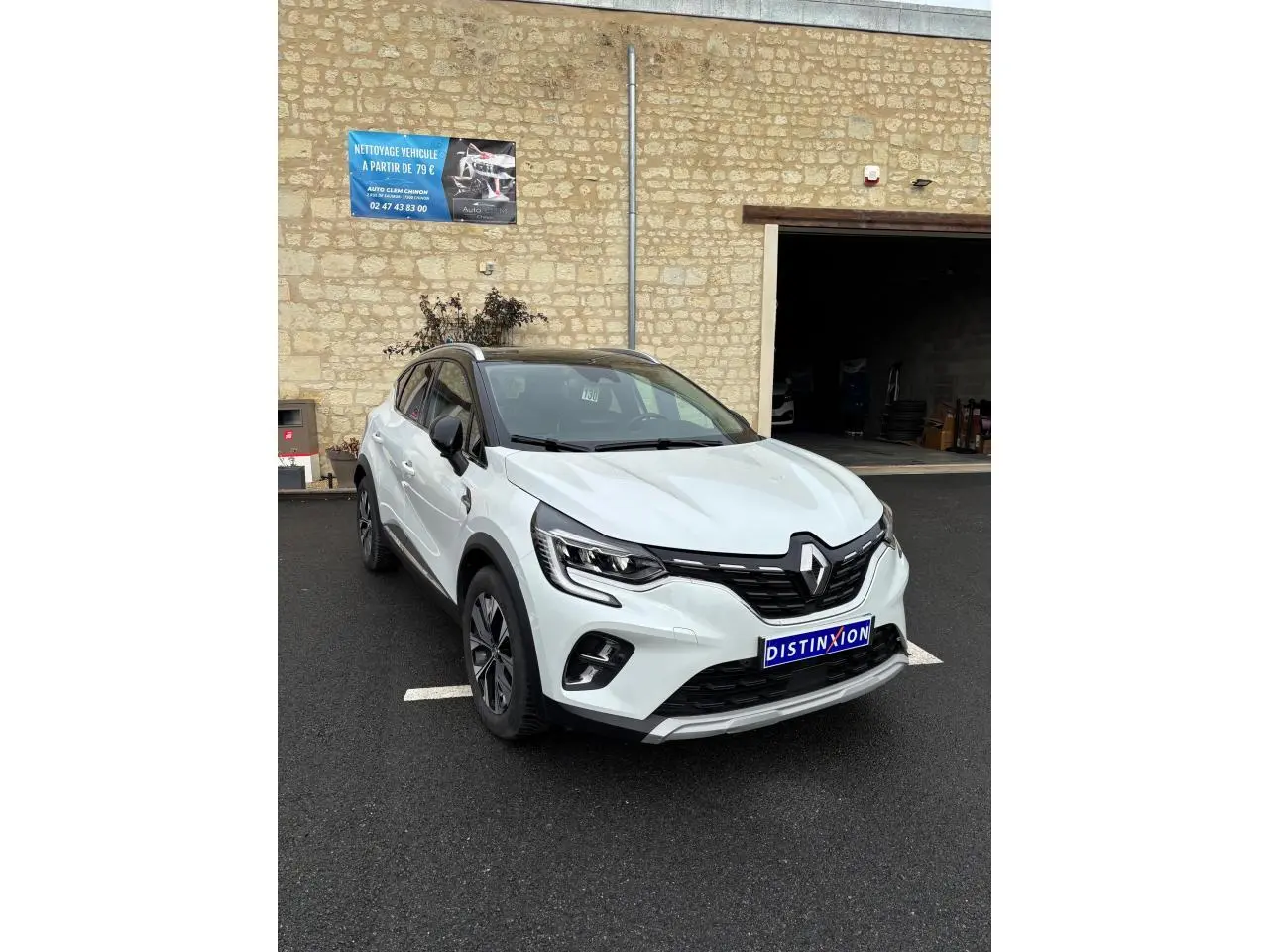 Renault Captur blanc en 3/4 avant droit, avec toit noir et détails noirs contrastants sur un parking extérieur.