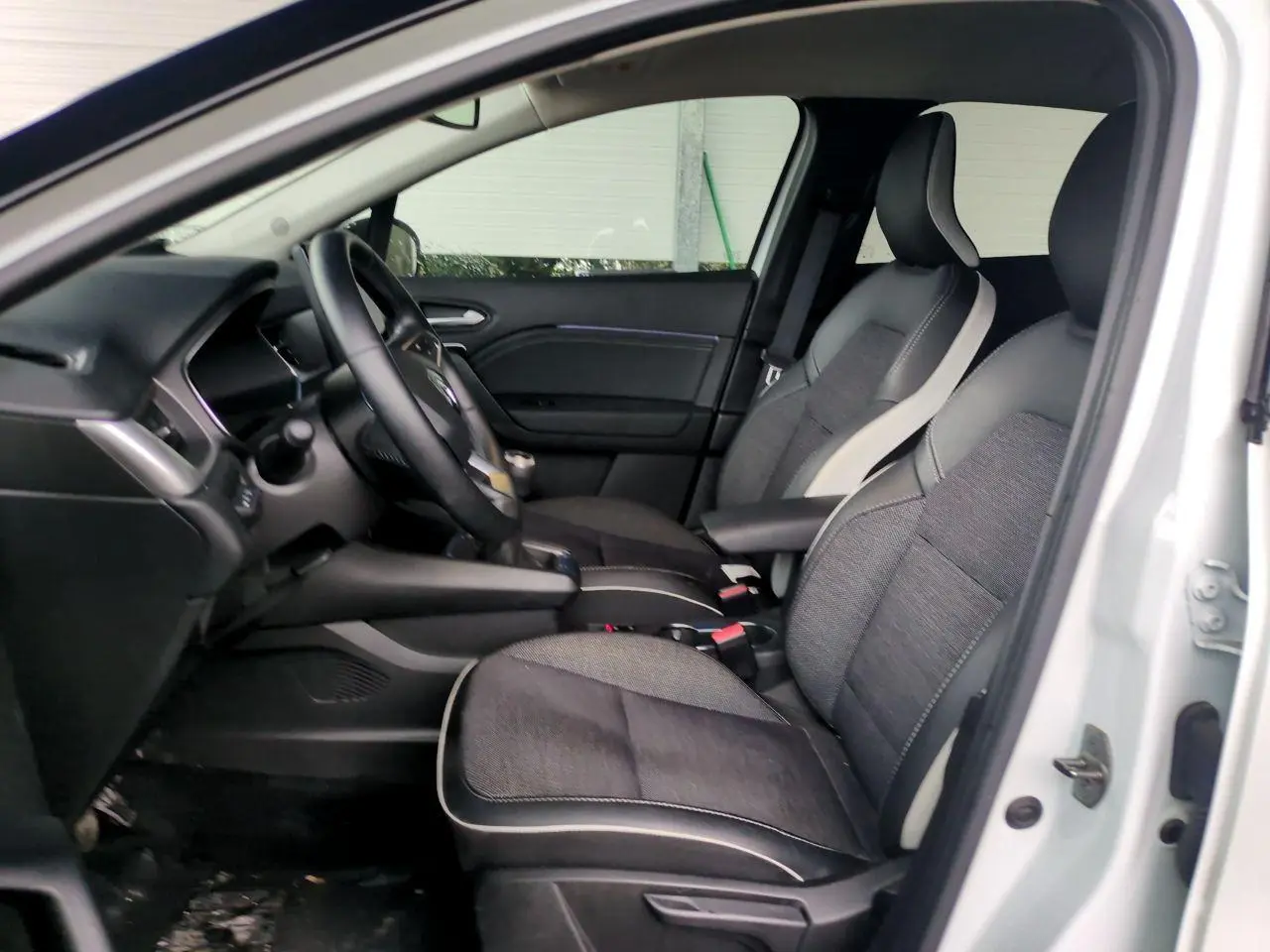 Vue intérieure côté gauche du Renault Captur blanc 2024, montrant les sièges avant bicolores et le volant.