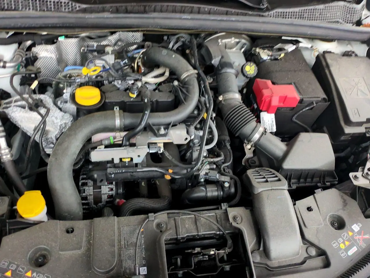 Moteur essence Renault Captur blanc 2024 vu de dessus, avec plusieurs bouchons jaunes et batterie à capuchon rouge.