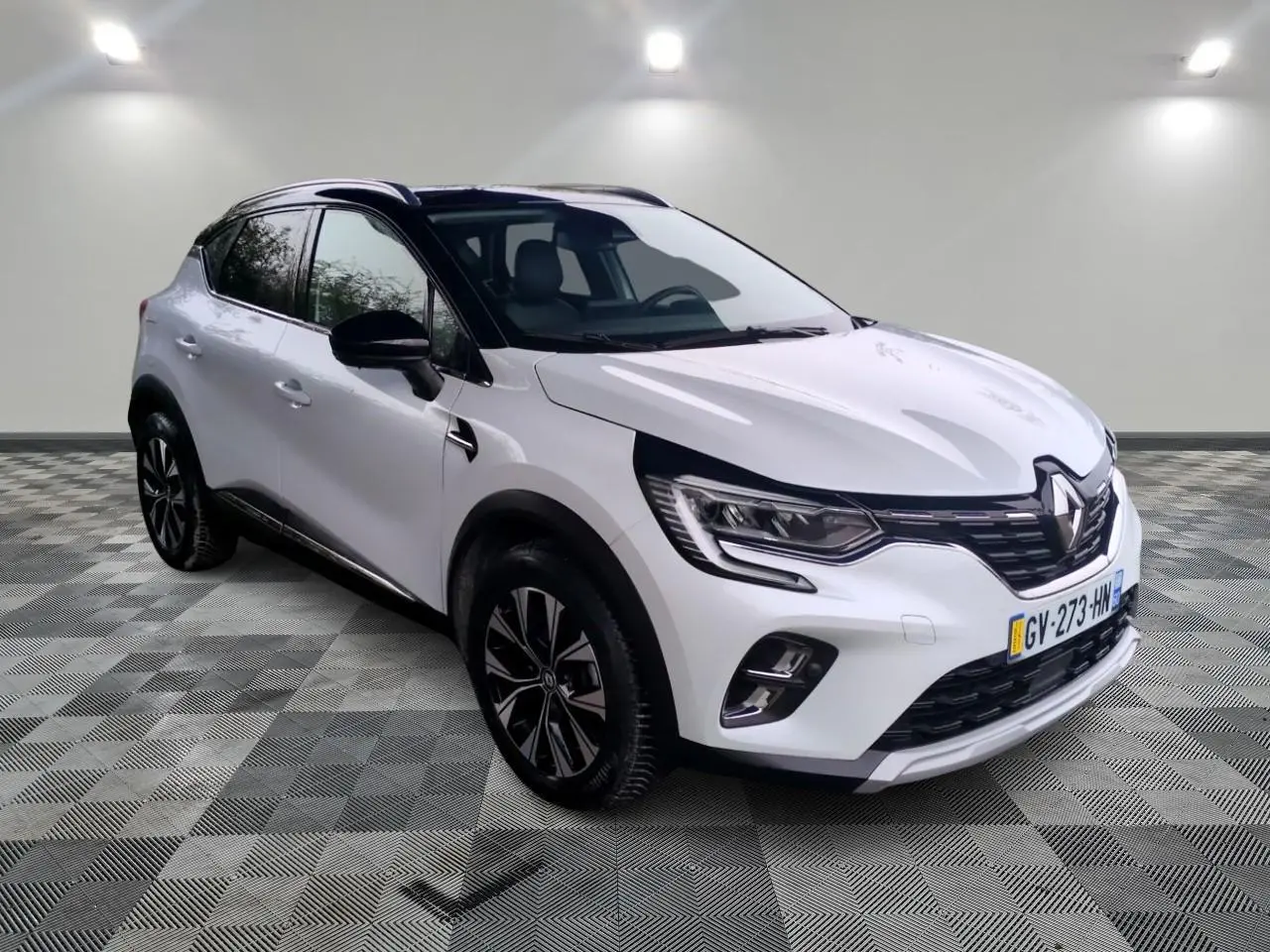 Renault Captur blanc en 3/4 avant droit, avec toit noir et jantes alliage bicolores sur fond neutre intérieur.