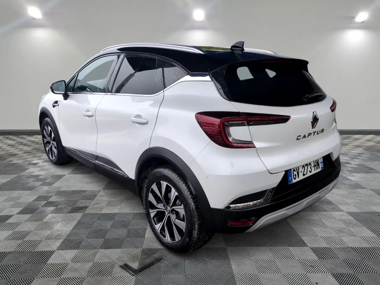 Vue 3/4 arrière droite du Renault Captur blanc avec toit noir et jantes alliage bicolores sur sol carrelé.
