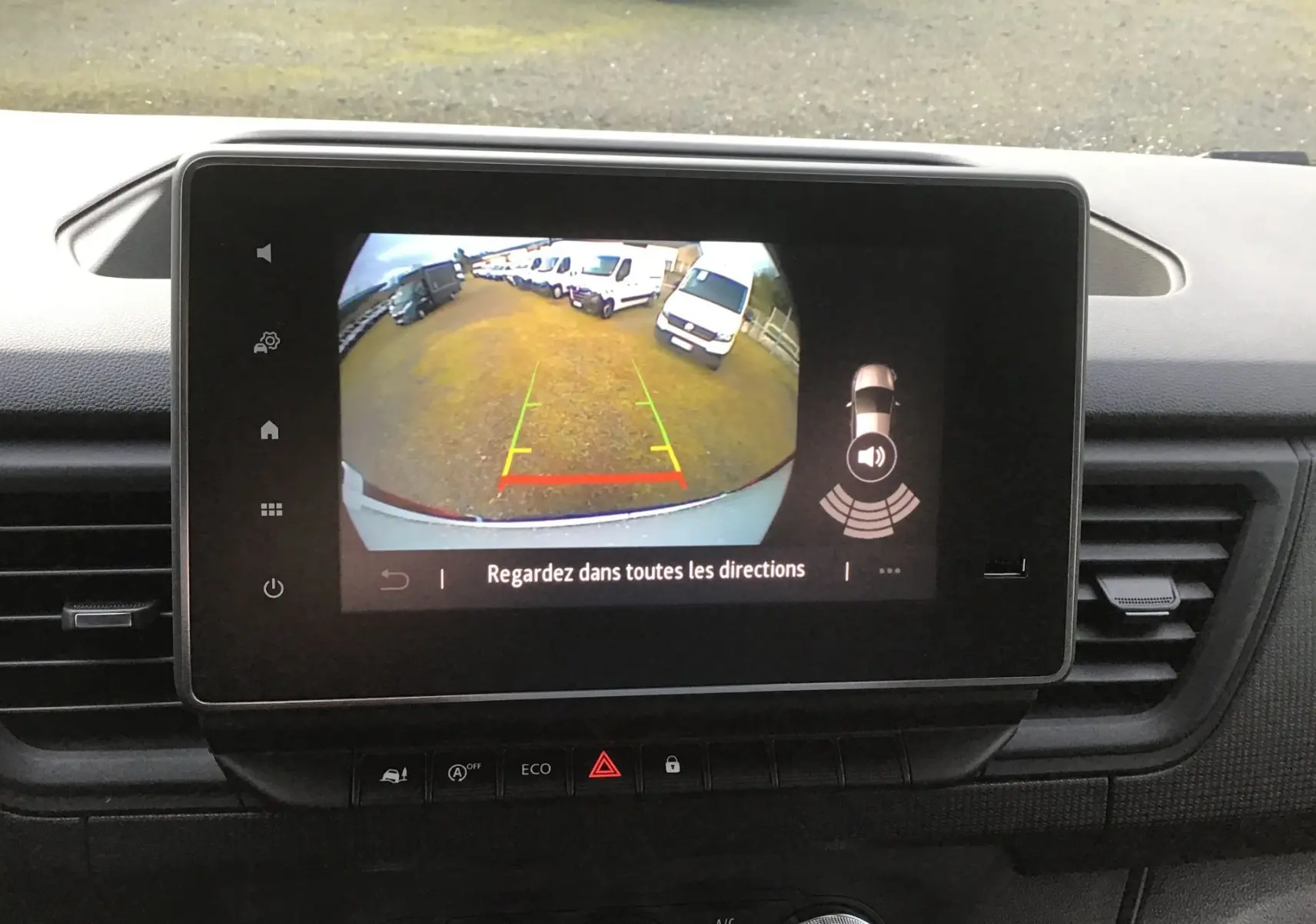 Écran tactile intérieur montrant la caméra de recul du Renault Trafic Fourgon blanc, avec alertes de proximité visibles.