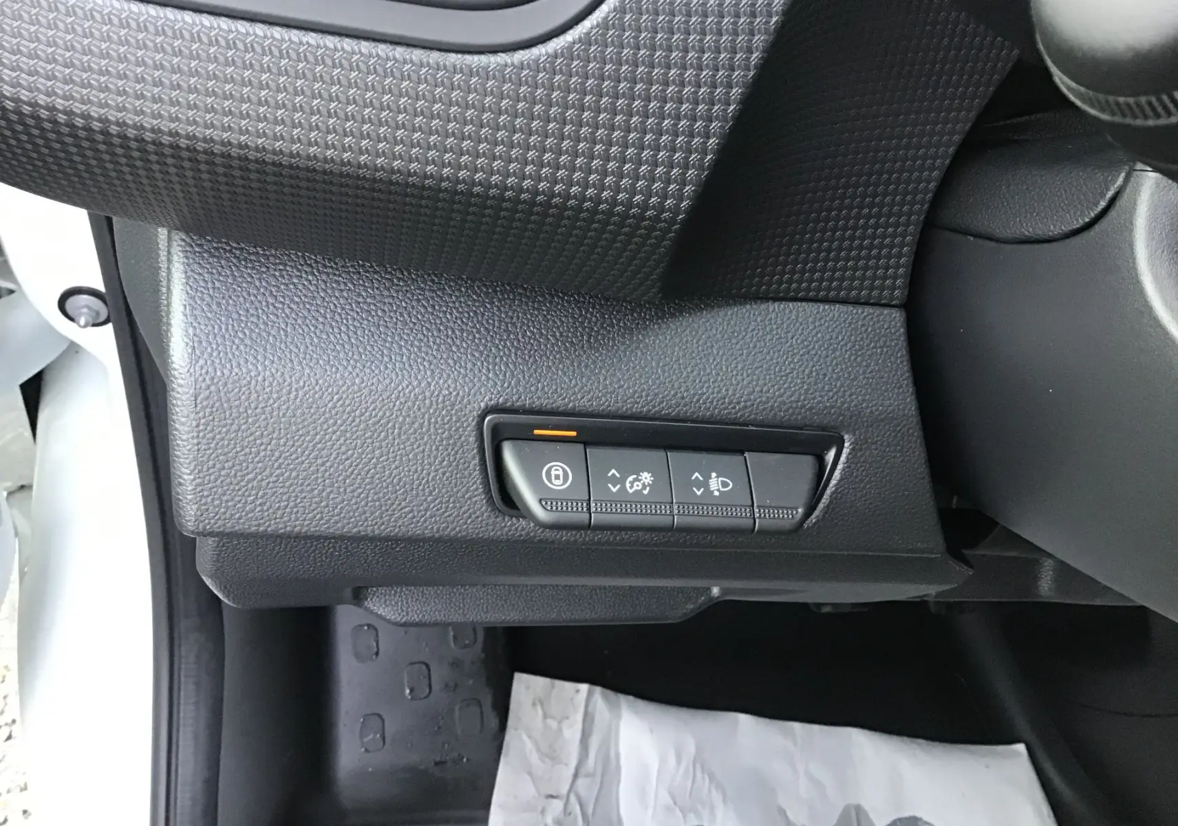 Gros plan sur les commandes de réglage d’éclairage et verrouillage, côté gauche du tableau de bord noir du Renault Trafic blanc.