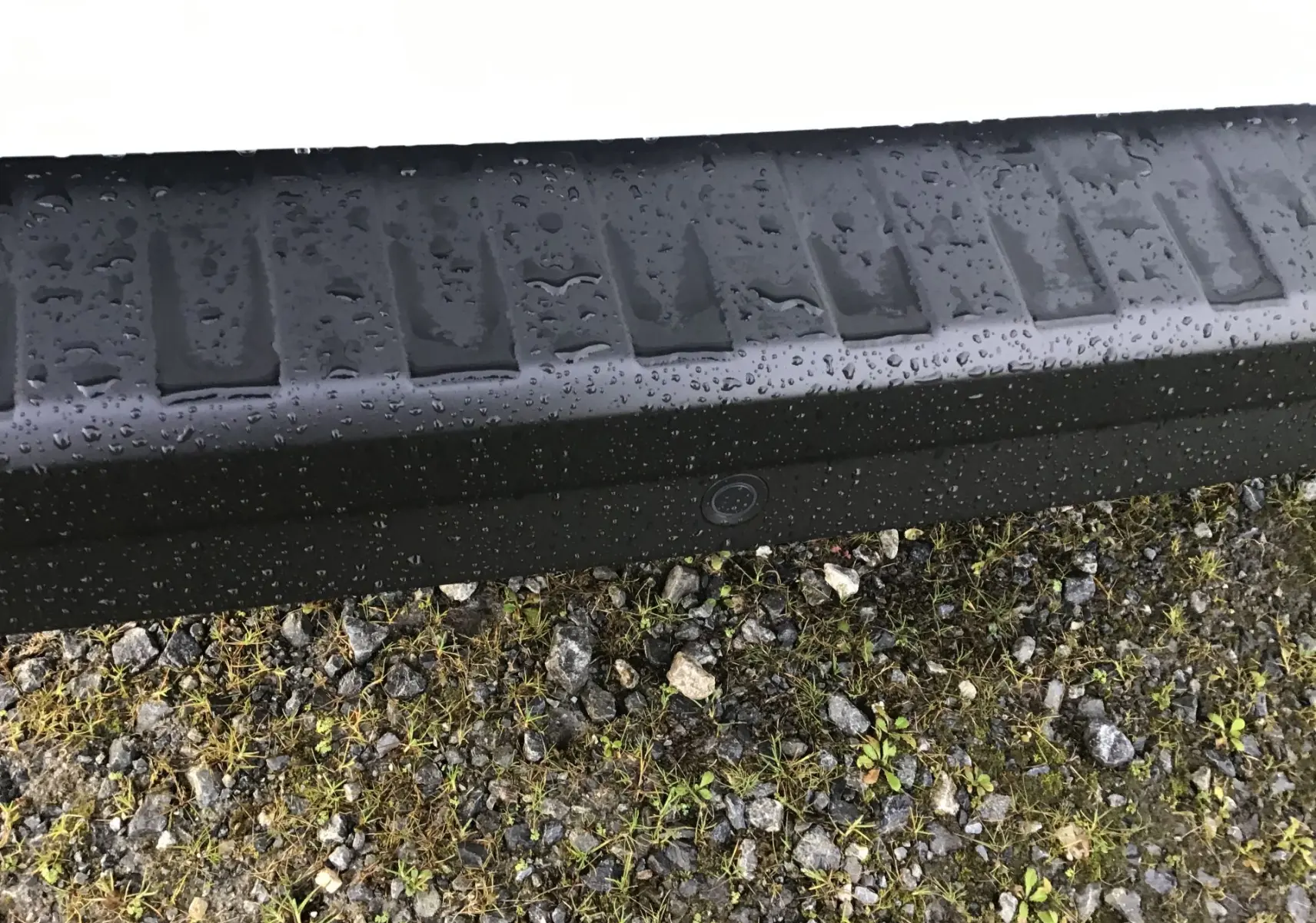 Gros plan sur le pare-chocs arrière noir avec caméra de recul du Renault Trafic Fourgon blanc, vue basse sur sol gravillonné.