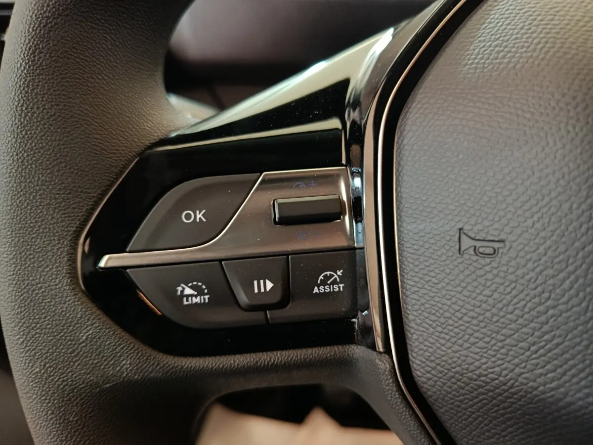 Gros plan sur les commandes gauche du volant noir du Peugeot Partner 2025, avec boutons de régulateur et assistance.