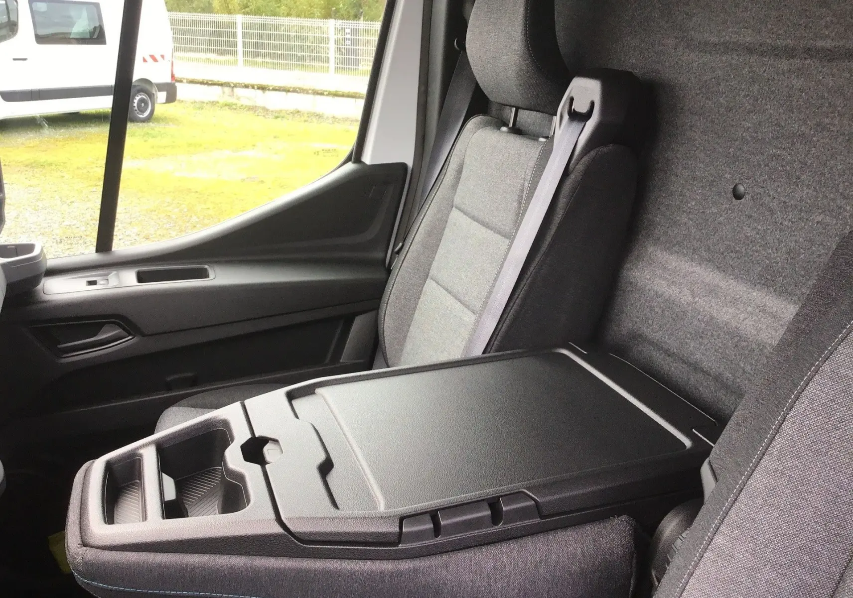 Intérieur du Renault Master blanc, vue côté passager montrant la banquette avec bureau mobile et accoudoir fermé.