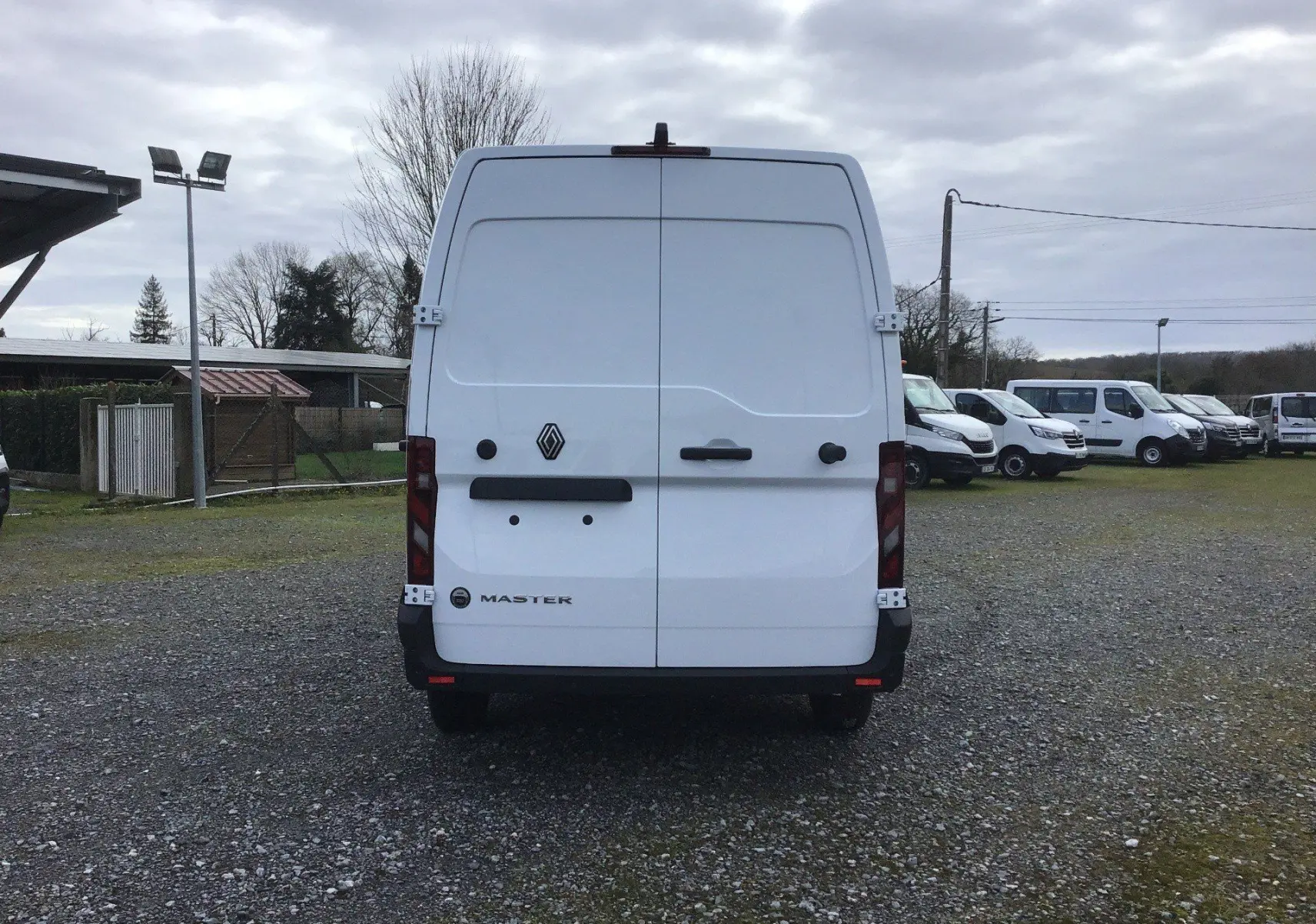 Vue arrière d’un utilitaire Renault Master blanc, portes arrière fermées, stationné sur un terrain gravillonné.