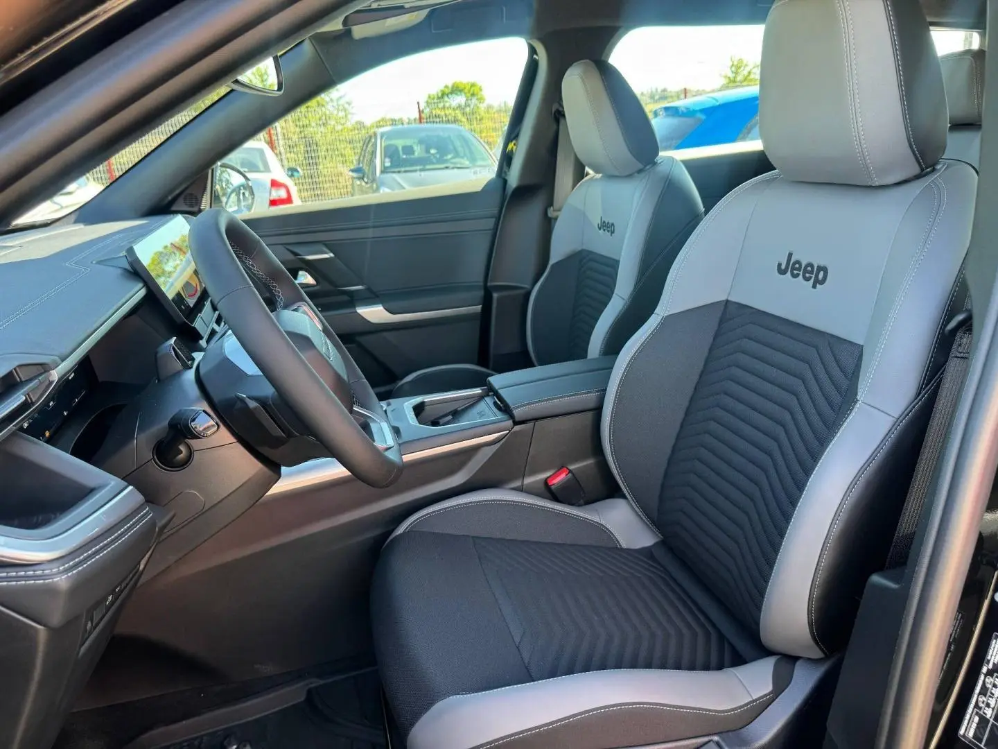 Vue intérieure côté conducteur du Jeep Compass 2026, sièges tissu gris/anthracite avec logo Jeep brodé.