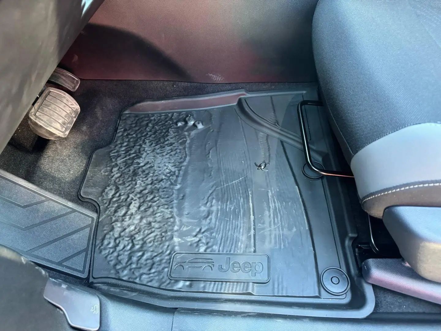 Gros plan sur le tapis de sol noir côté conducteur du Jeep Compass 2026 avec logo Jeep visible au pied du siège gris anthracite.