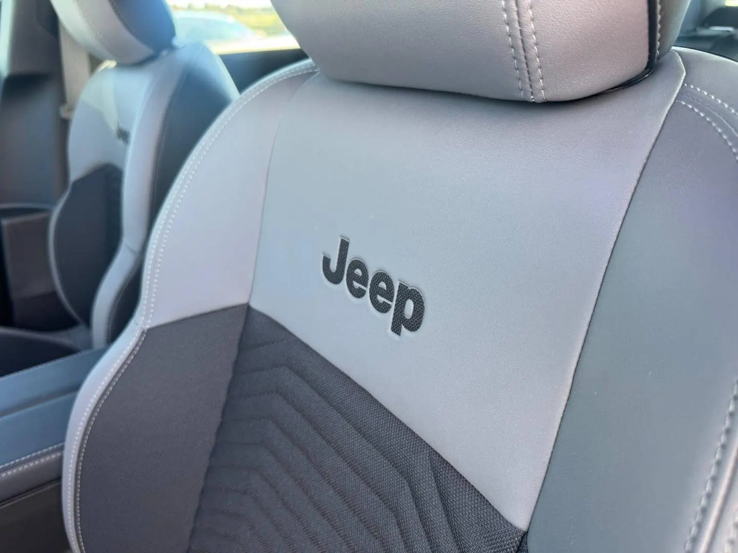 Gros plan sur le siège avant gris et anthracite avec logo Jeep brodé, mettant en valeur la finition intérieure du Compass.
