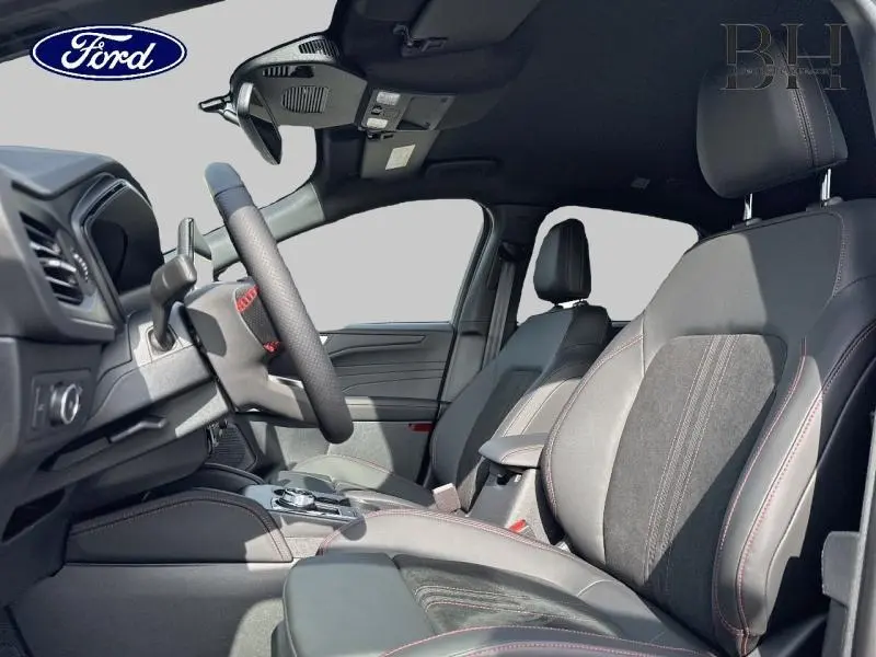 Intérieur avant du Ford Kuga 2025, sièges sport noirs avec surpiqûres rouges, volant multifonction visible de côté gauche.